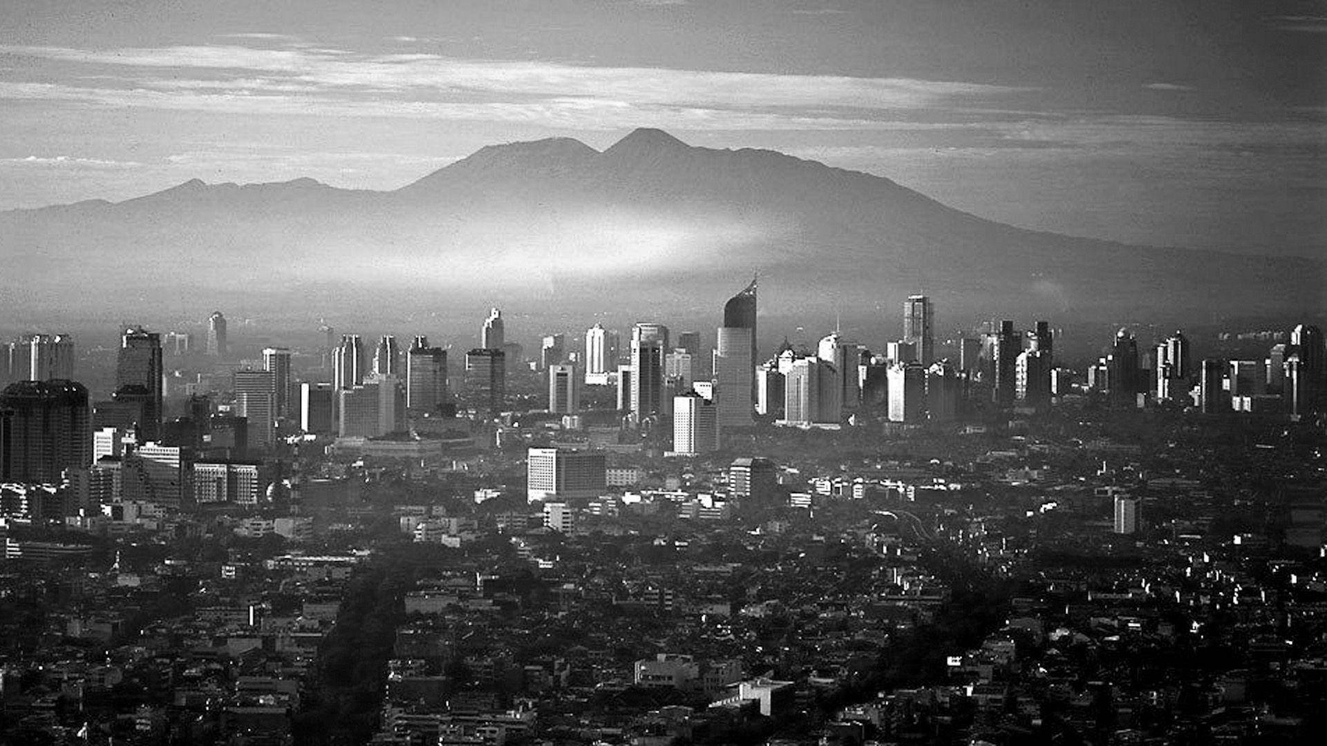 Jakarta 桌布 壁紙 — 多雲天空下，摩天大樓與遠山構成的單色城市景觀。