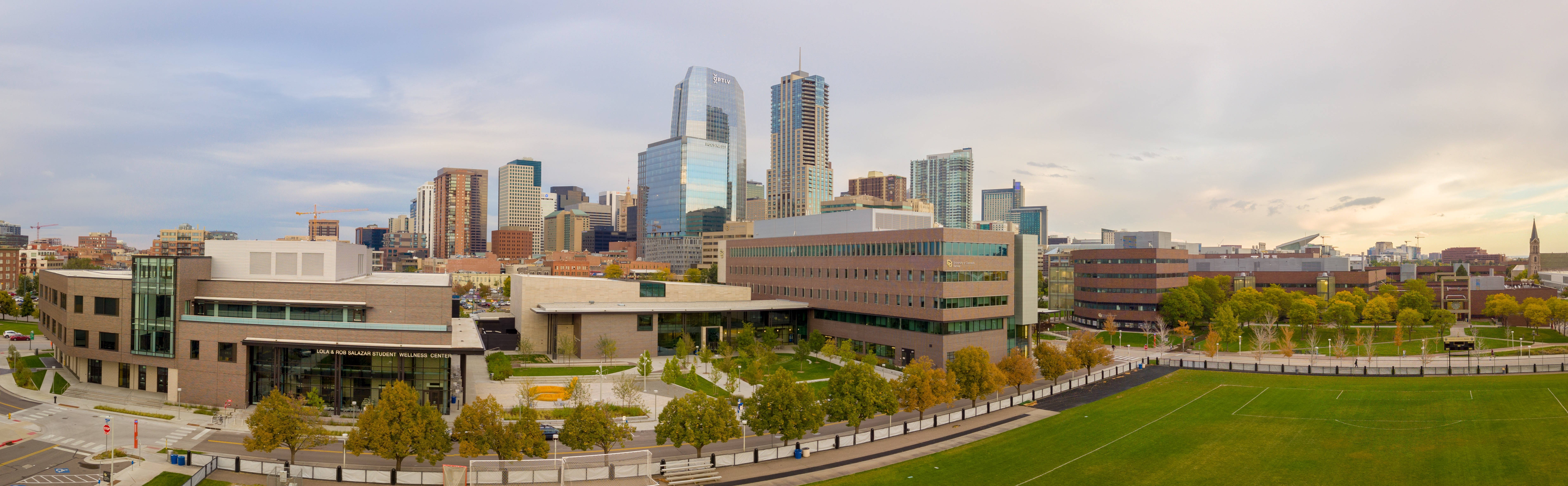 Denver 桌布 壁紙 — 多雲天空下，現代城市景觀的全景視圖，包括玻璃摩天大樓和綠色運動場。