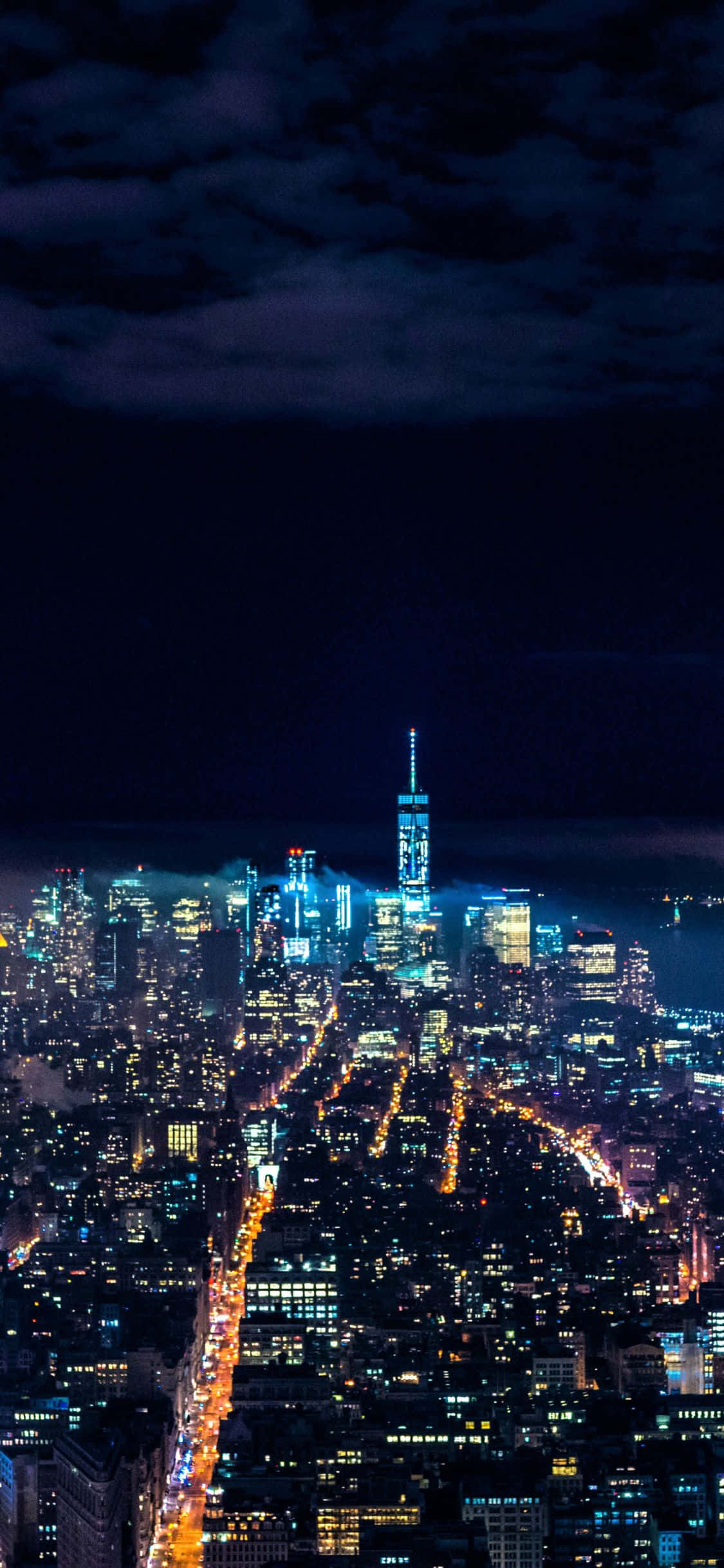 iPhone X New York 桌布 壁紙 — 多雲天空下，紐約市天際線的夜間航拍景觀，閃爍的摩天大樓和燈火通明的街道。