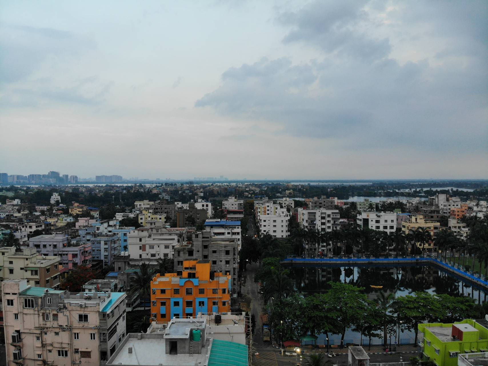 Kolkata 桌布 壁紙 — 多雲天空下，色彩繽紛的建築物和反射水體構成的廣闊城市景觀。