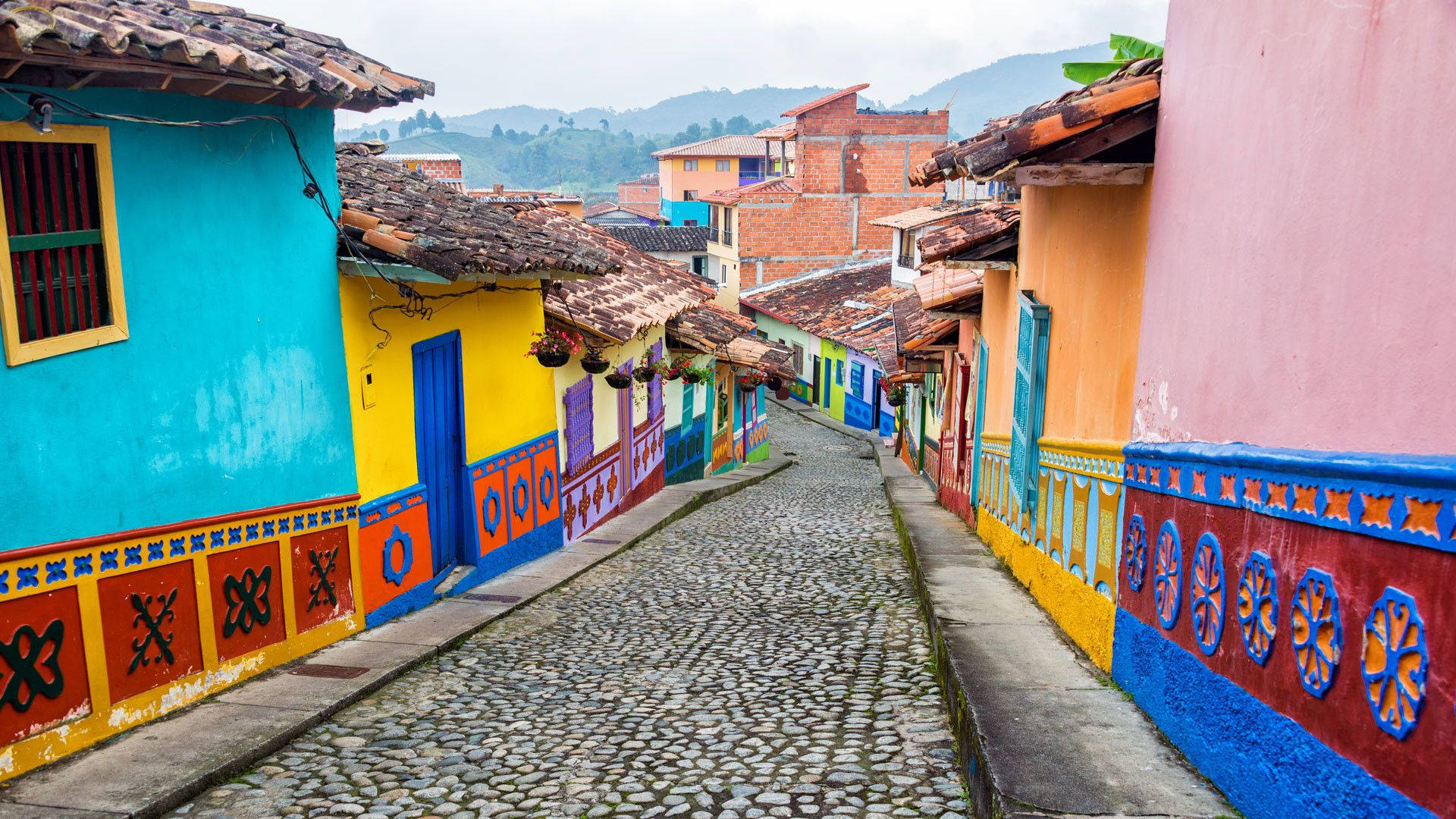 Colombia 桌布 壁紙 — 多雲天空下，色彩繽紛的殖民風格房屋排列在充滿活力的鵝卵石街道上。