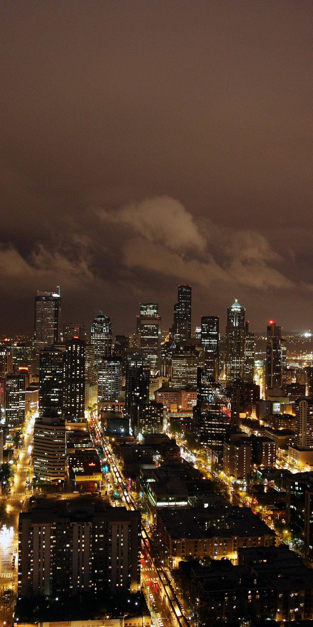 City At Night 桌布 壁紙 — 多雲天空下，閃爍摩天大樓和街燈的廣闊城市景觀的鳥瞰夜景。
