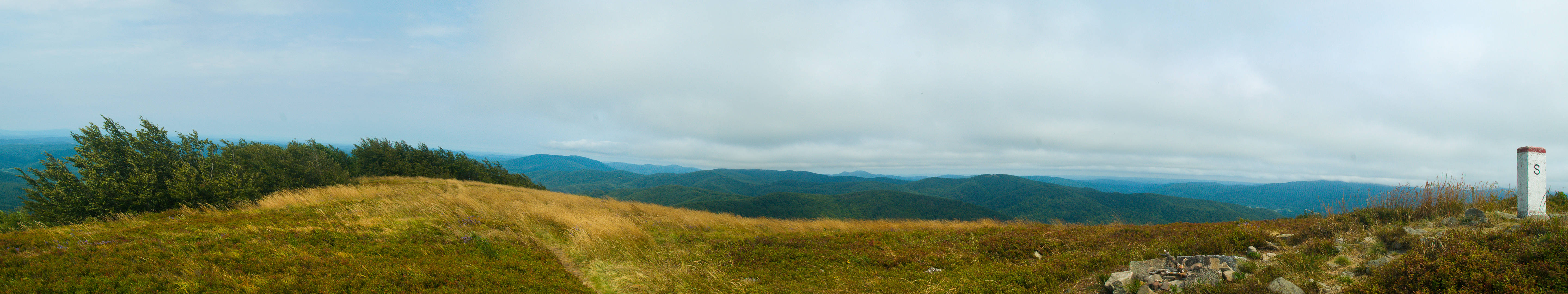 windy 桌布 壁紙 — 多雲天空下連綿起伏的綠色山丘全景，右側有一個小小的白色標記。