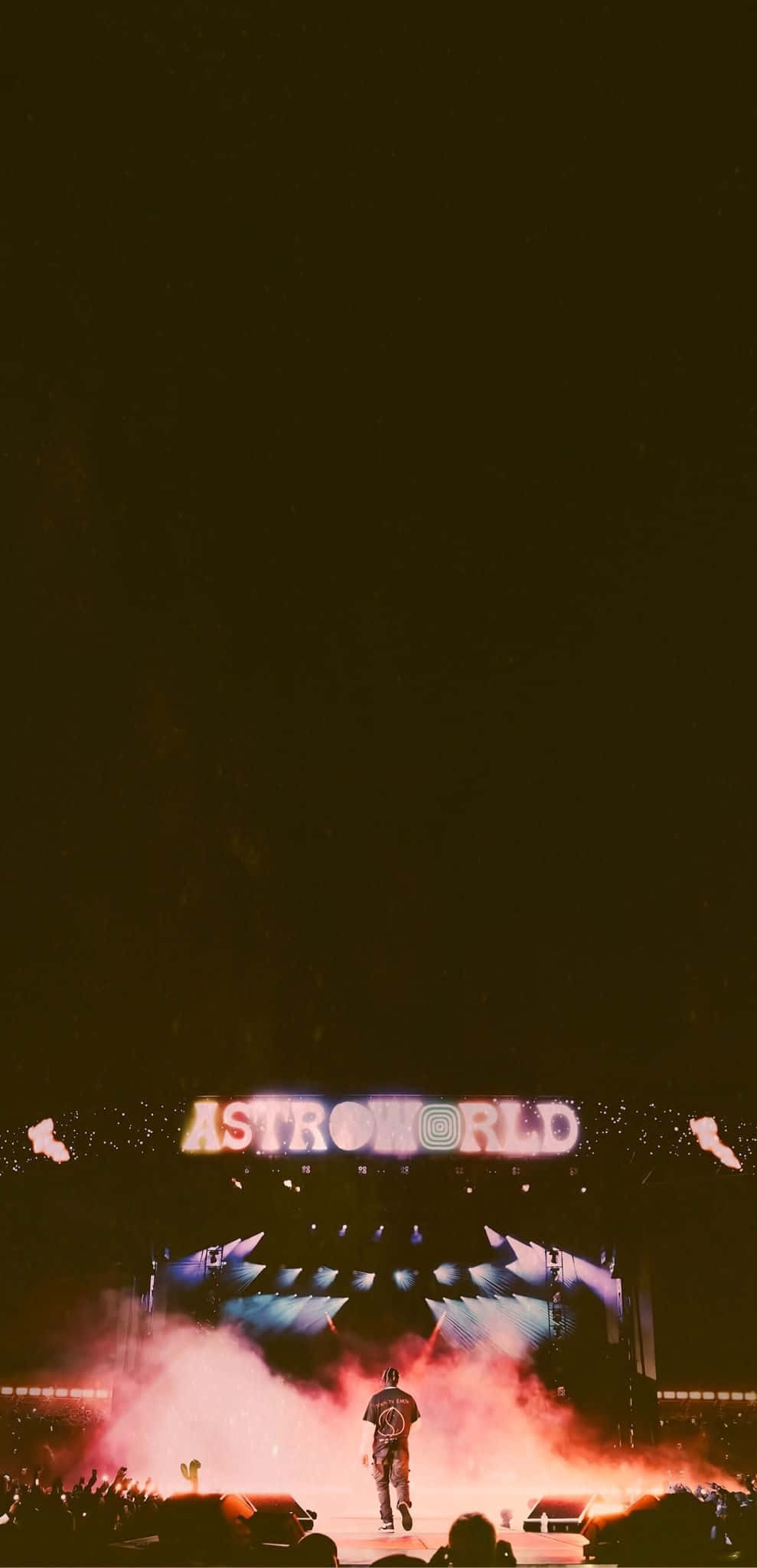 Astroworld 桌布 壁紙 — 夜晚，一位表演者獨自站在煙霧瀰漫的演唱會舞台上，下方是發光的「ASTROWORLD」標誌。
