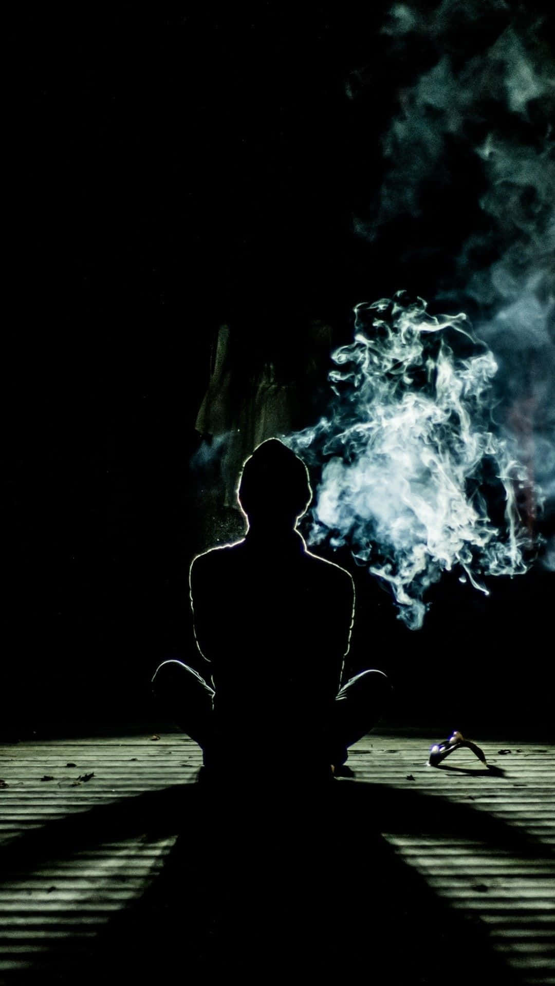 Meditation iPhone 桌布 壁紙 — 夜晚，一個人盤腿坐在木地板上，發光的煙霧在他們周圍旋轉的剪影。