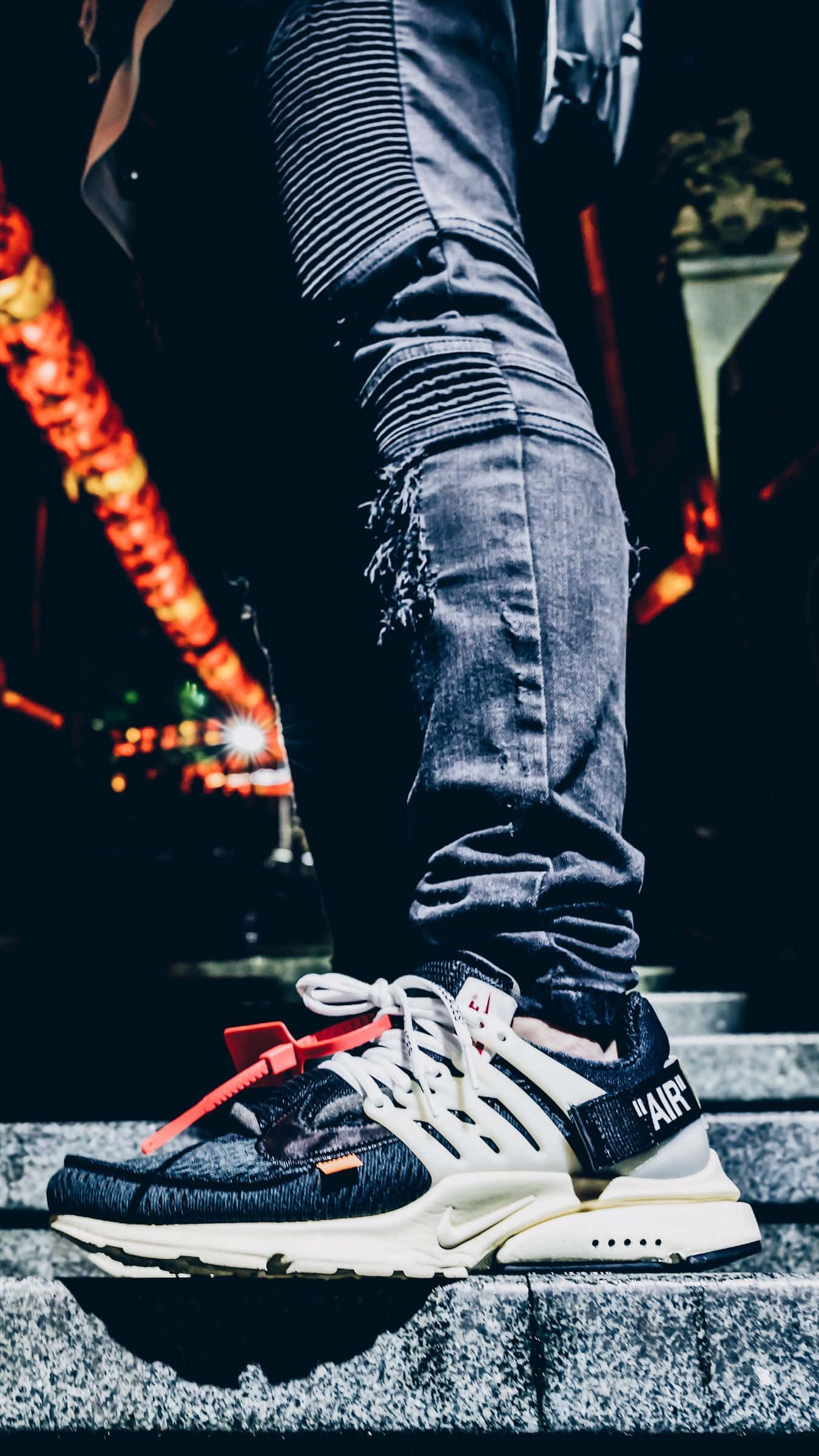 Sneaker 桌布 壁紙 — 夜晚，一個人穿著紅鞋帶的黑白運動鞋站在石階上，背景有發光的橙色燈光，腳部特寫。