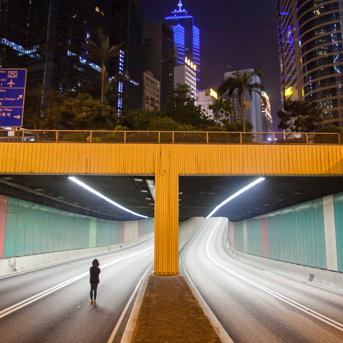 City At Night 桌布 壁紙 — 夜晚，一個孤獨的身影在發光的黃色天橋下行走，霓虹燈閃爍的摩天大樓聳立在上方。