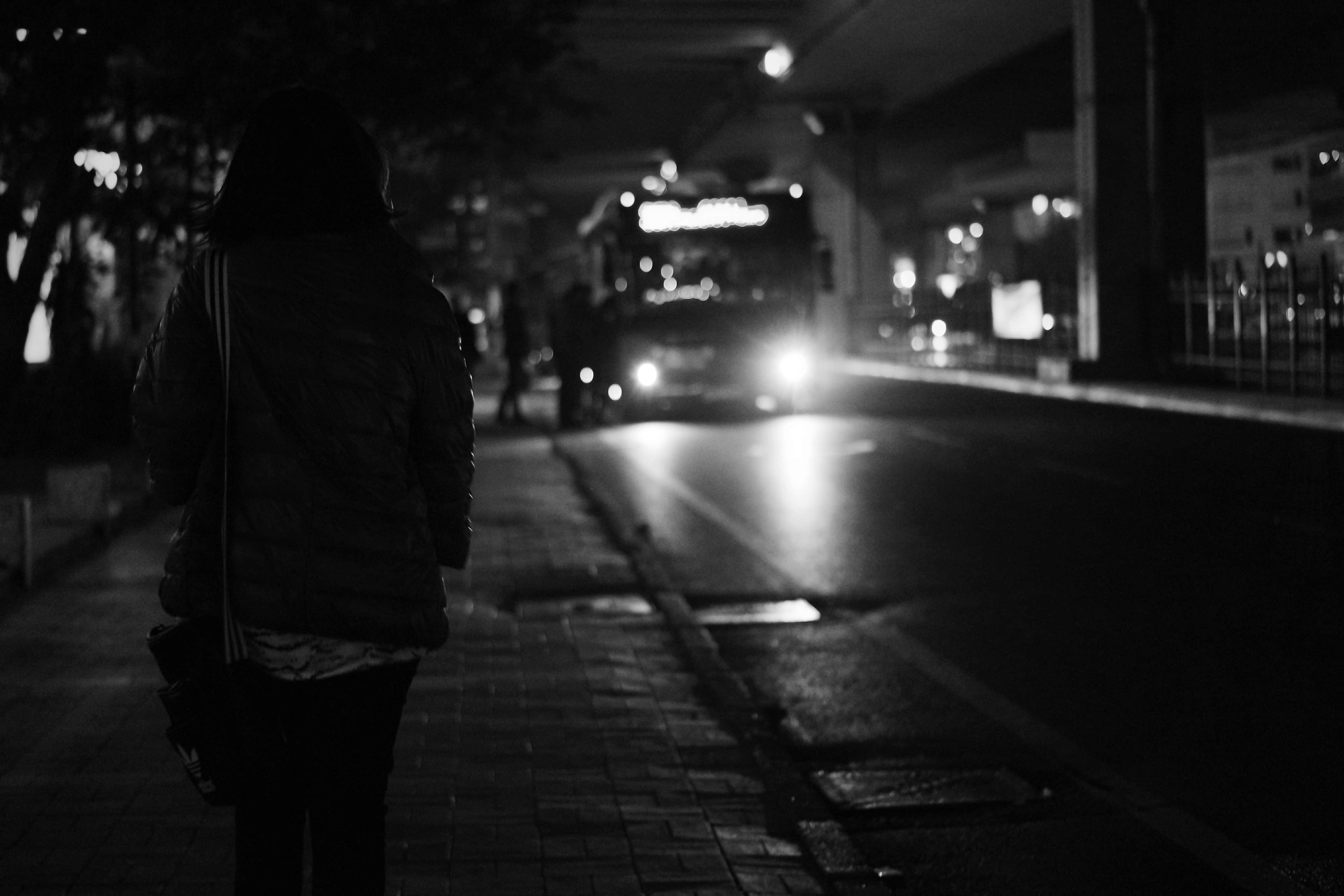 Black And White Street 桌布 壁紙 — 夜晚，一個孤獨的身影沿著濕漉漉的城市人行道行走，一輛巴士正亮著車頭燈駛近。