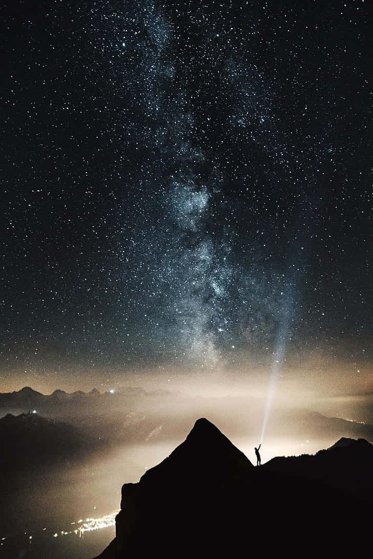自然 桌布 壁紙 — 夜晚，一個孤獨的身影站在山頂，將手電筒向上照向銀河系。