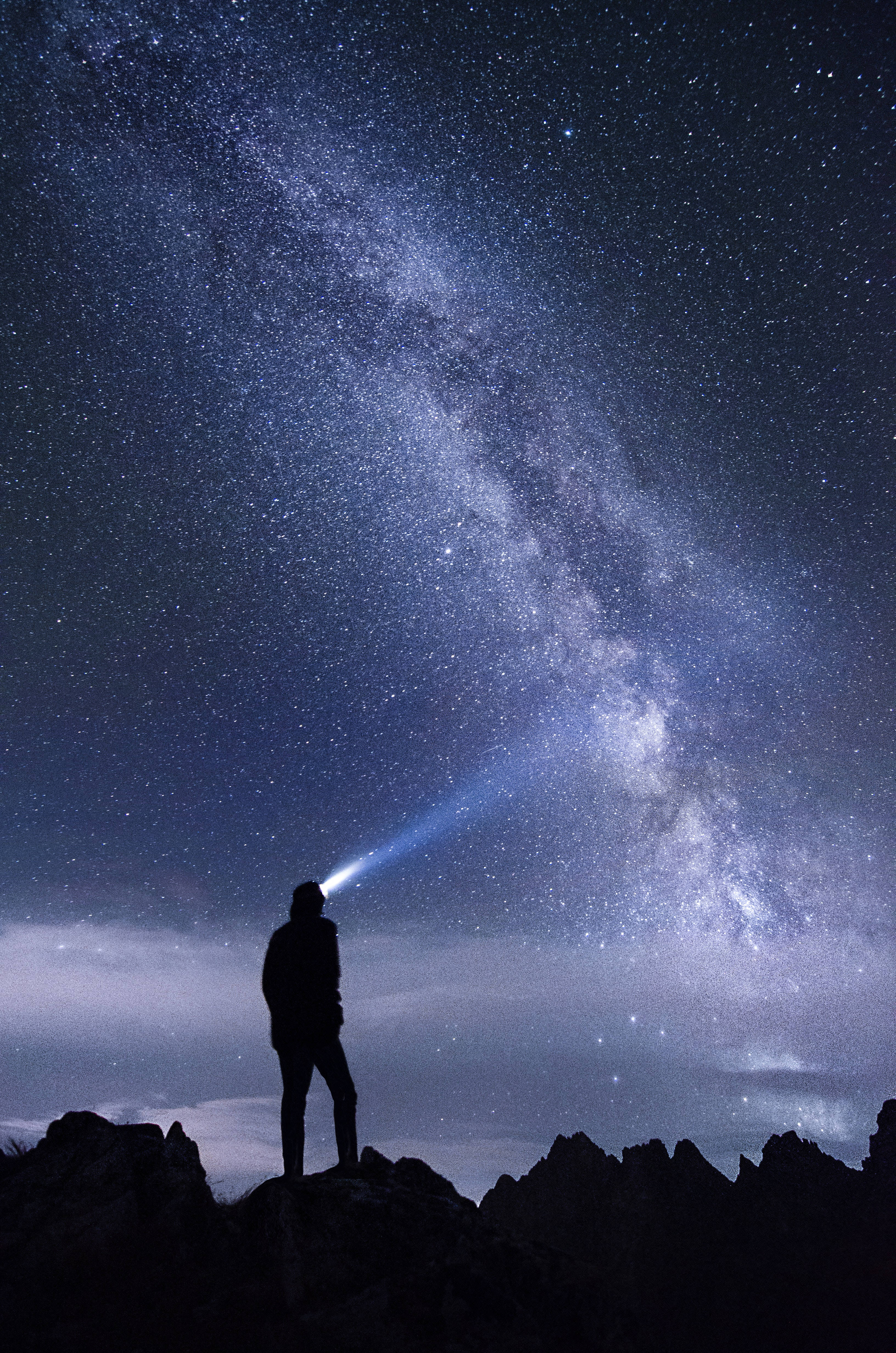 夜空 桌布 壁紙 — 夜晚，一個孤獨的身影站在岩石山頂上，將手電筒照向銀河系。