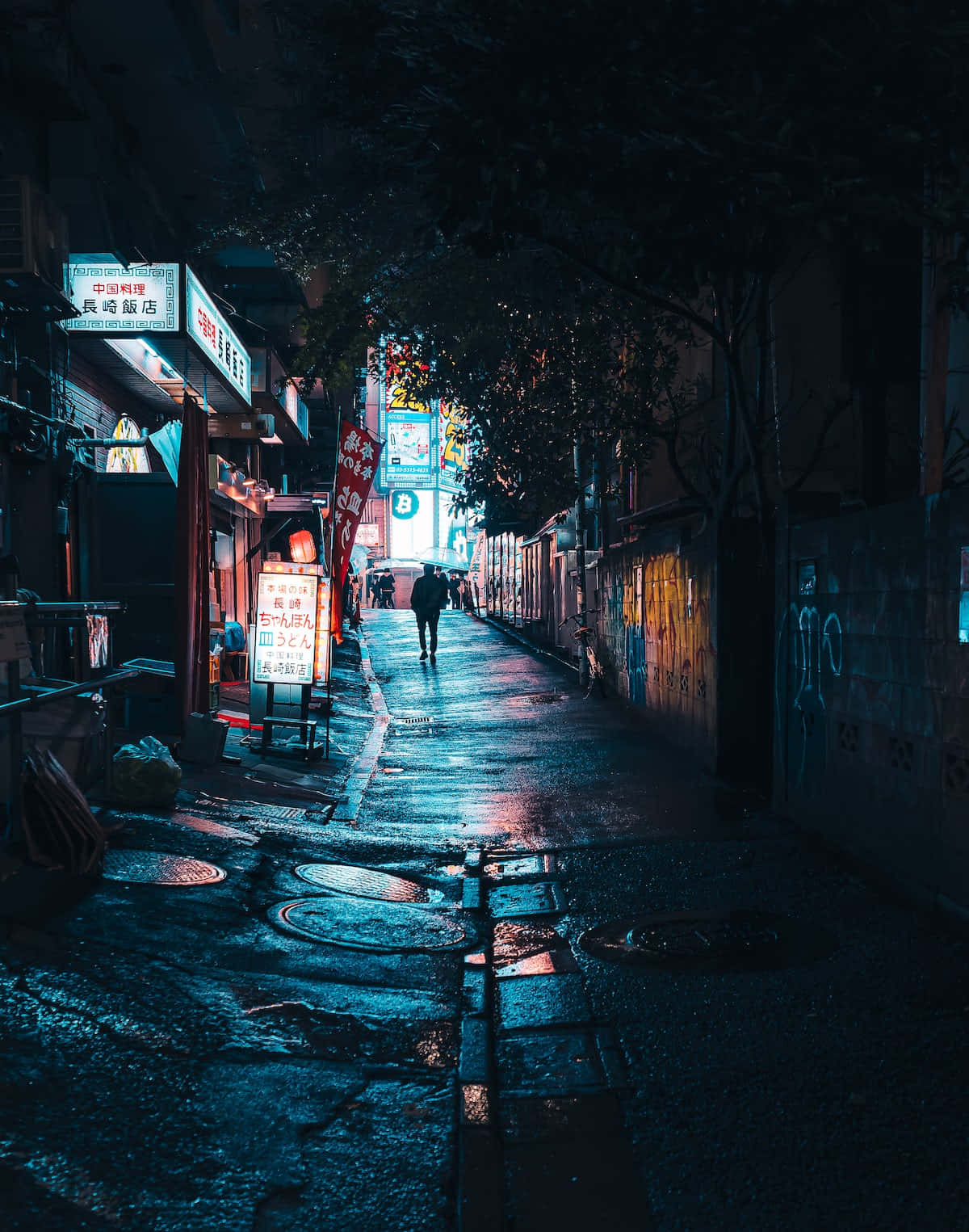 Dark Alleyway 桌布 壁紙 — 夜晚，一個孤獨的身影走在一條霓虹燈閃爍的小巷中，潮濕的路面反射著周圍商店鮮豔的藍色和紅色燈光。