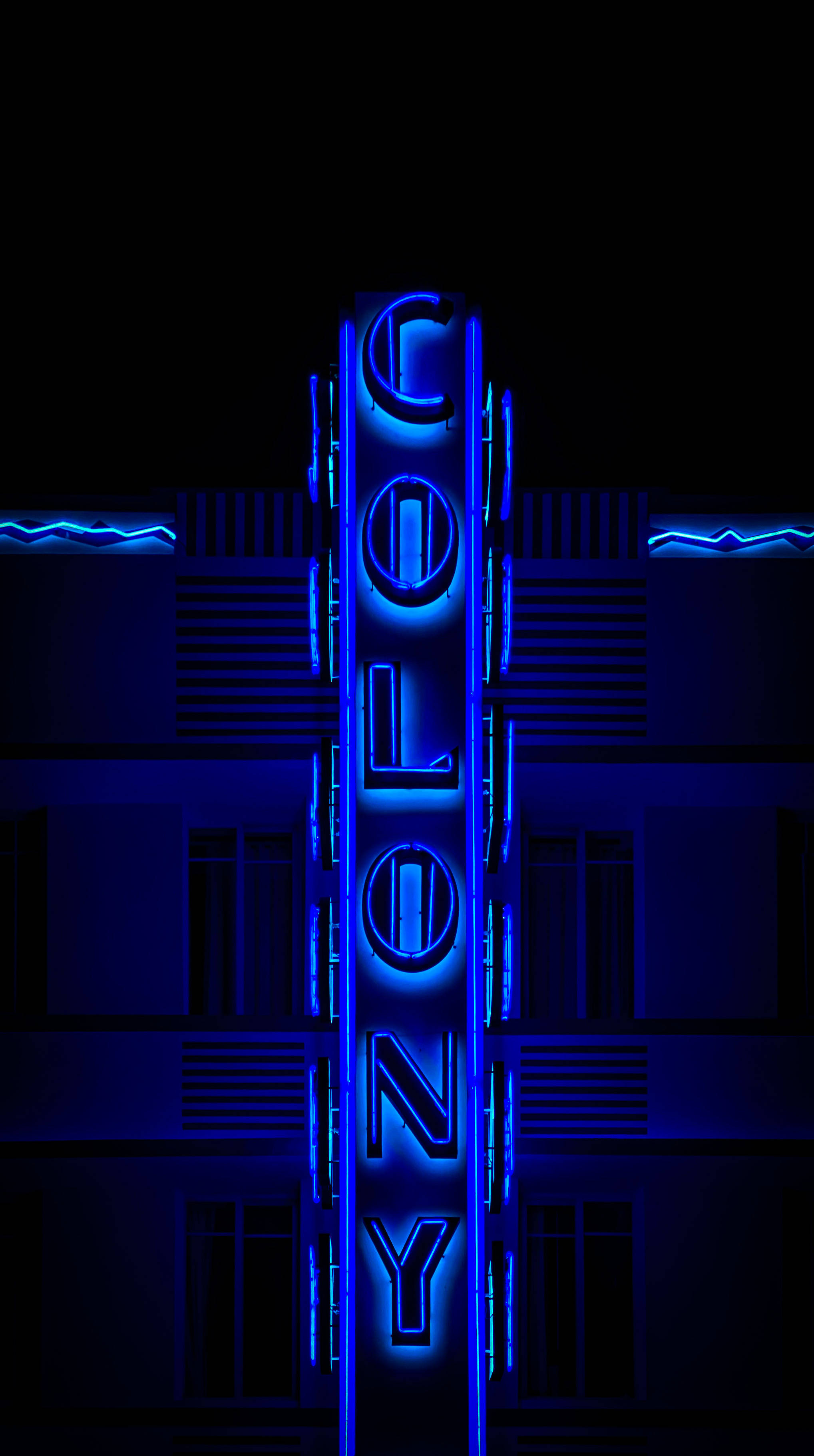 霓虹美學 桌布 壁紙 — 夜晚，一個高聳的藍色霓虹燈牌拼出COLONY，在黑暗的建築物外牆上閃耀。