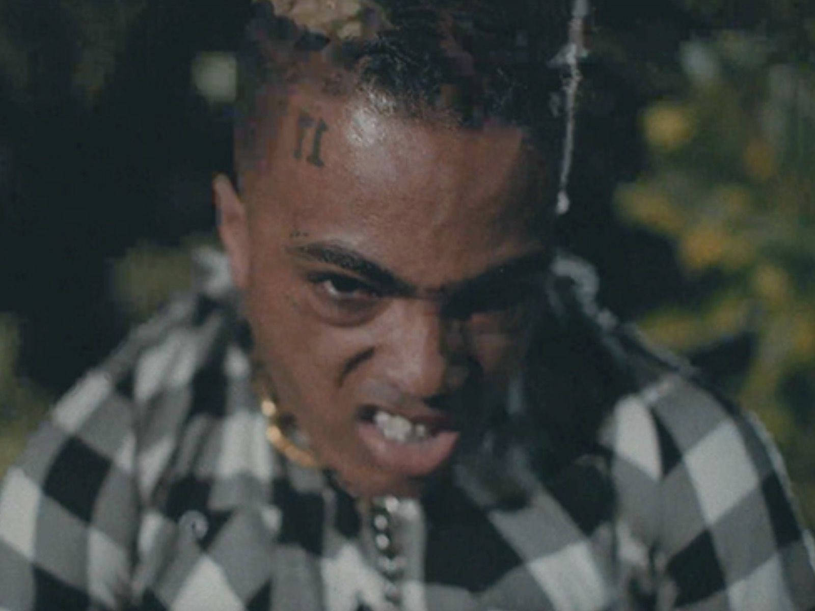 XXXTENTACION 桌布 壁紙 — 夜晚，一名額頭上有羅馬數字刺青的男子穿著黑白格紋襯衫的特寫。
