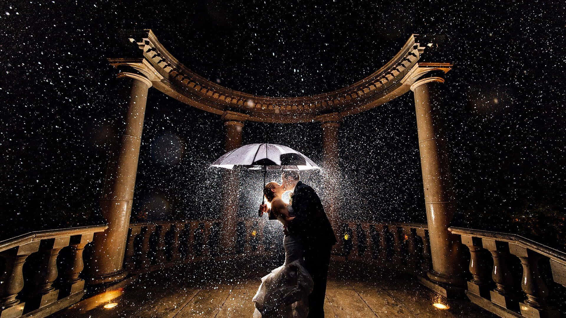 Bride And Groom 桌布 壁紙 — 夜晚，一對情侶在發光的雨傘下接吻，雪花飄落在他們周圍，下方是宏偉的石拱門。