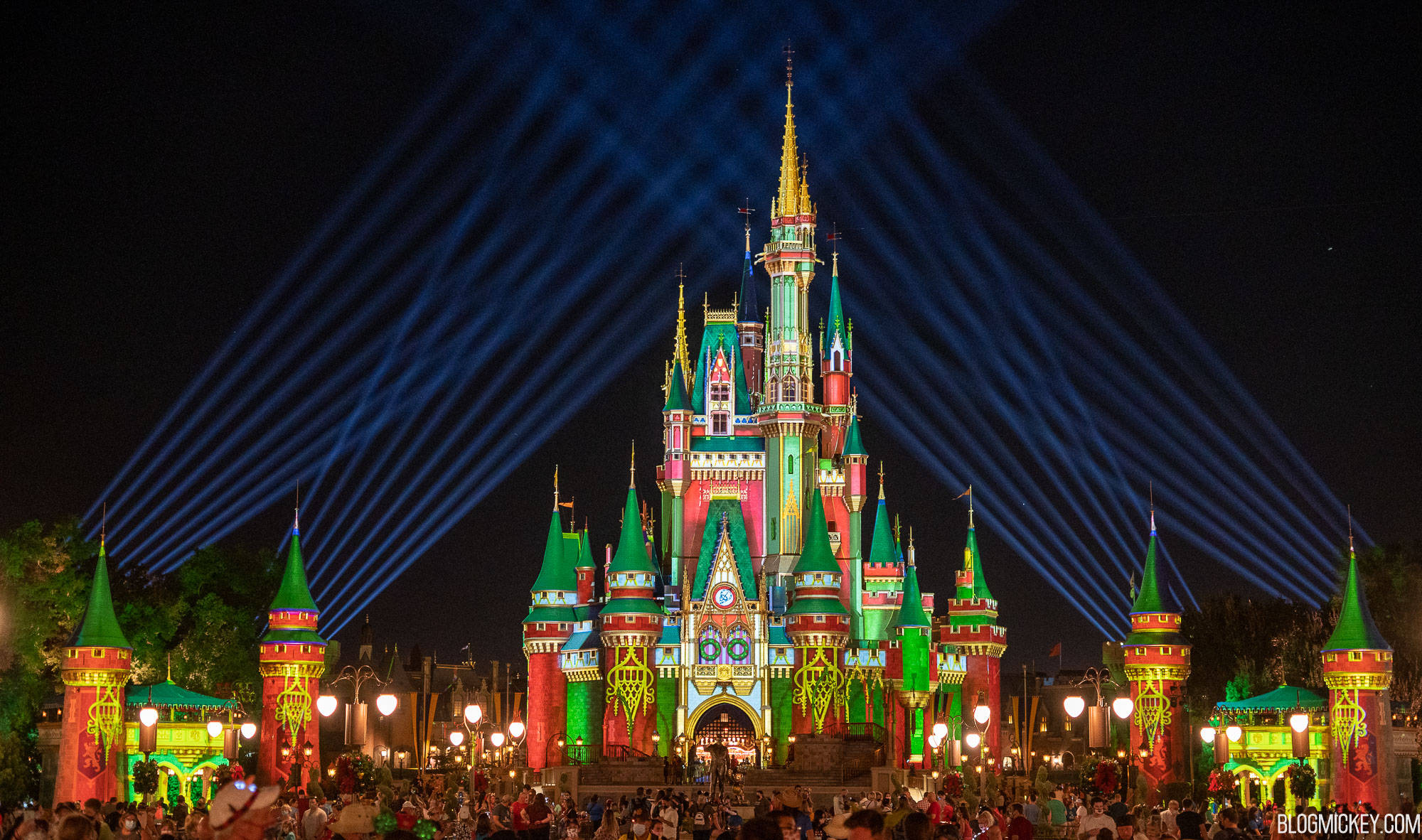 Disneyland Castle 桌布 壁紙 — 夜晚，一座宏偉的城堡在戲劇性的藍色雷射光束下，被鮮豔的紅、綠、金色燈光照亮。