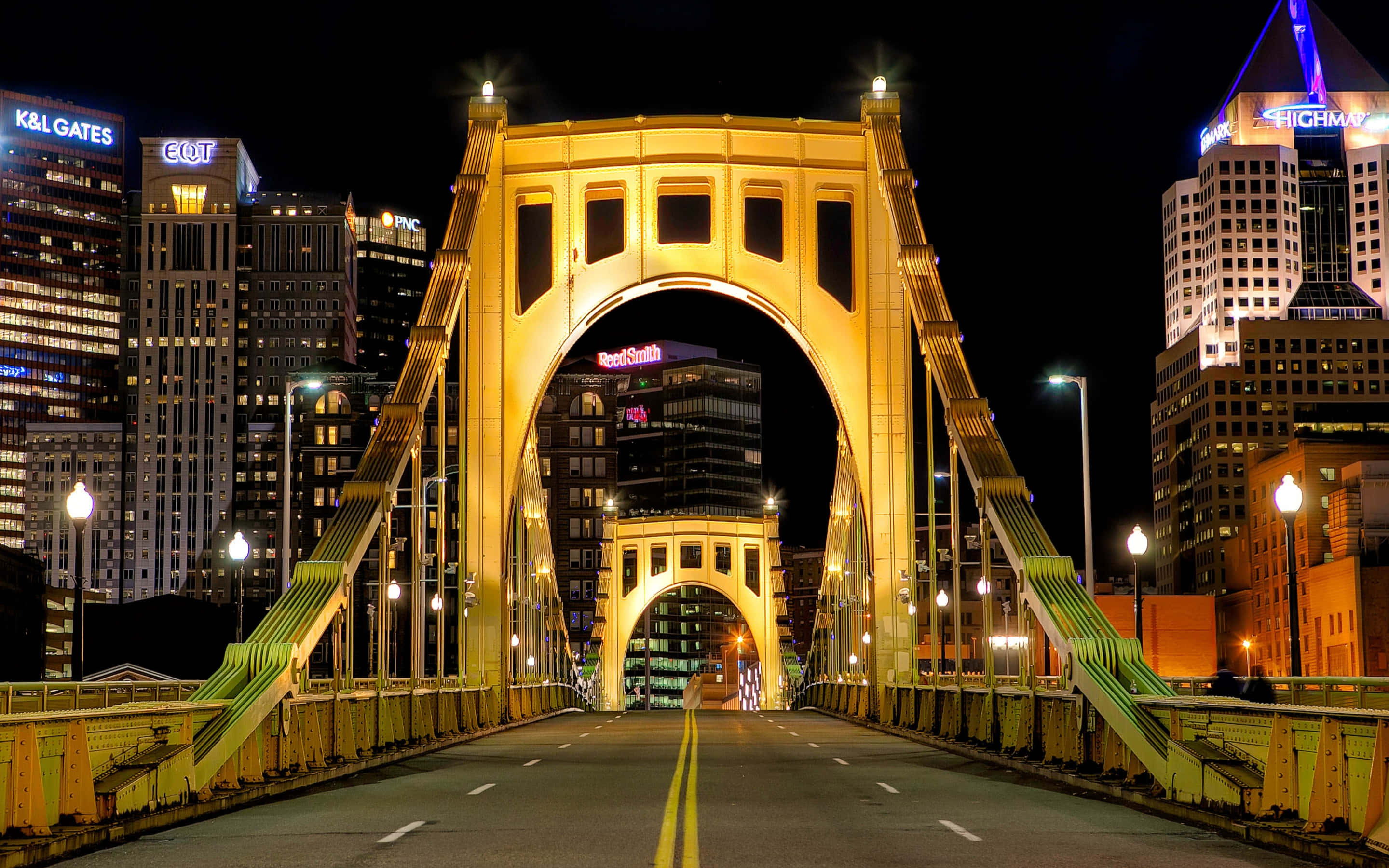 Pittsburgh Skyline 桌布 壁紙 — 夜晚，一座宏偉的照明橋樑拱跨在黑暗的城市街道上，背景是閃爍的摩天大樓。