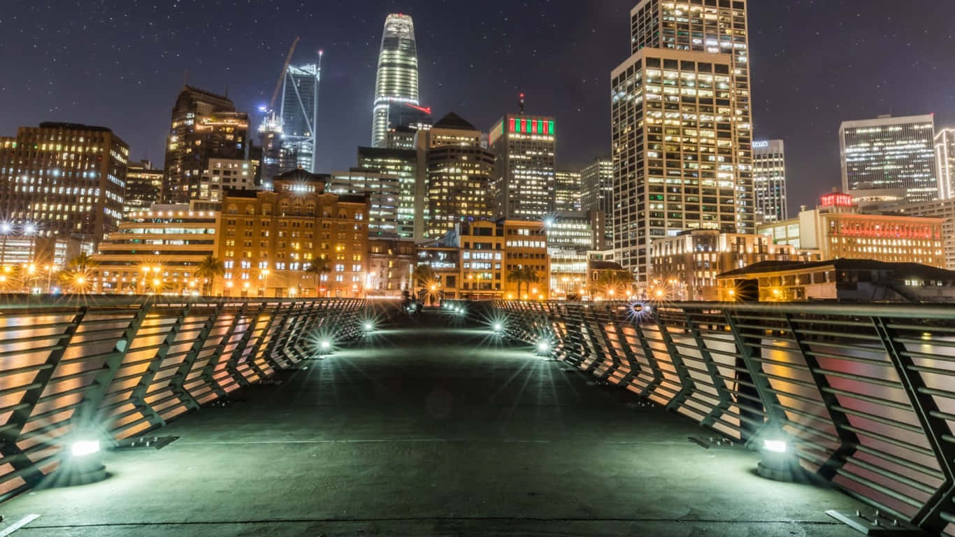 1366x768 San Francisco 桌布 壁紙 — 夜晚，一座現代橋樑通向在星空下閃耀的城市天際線，伴隨著車輛的光跡。