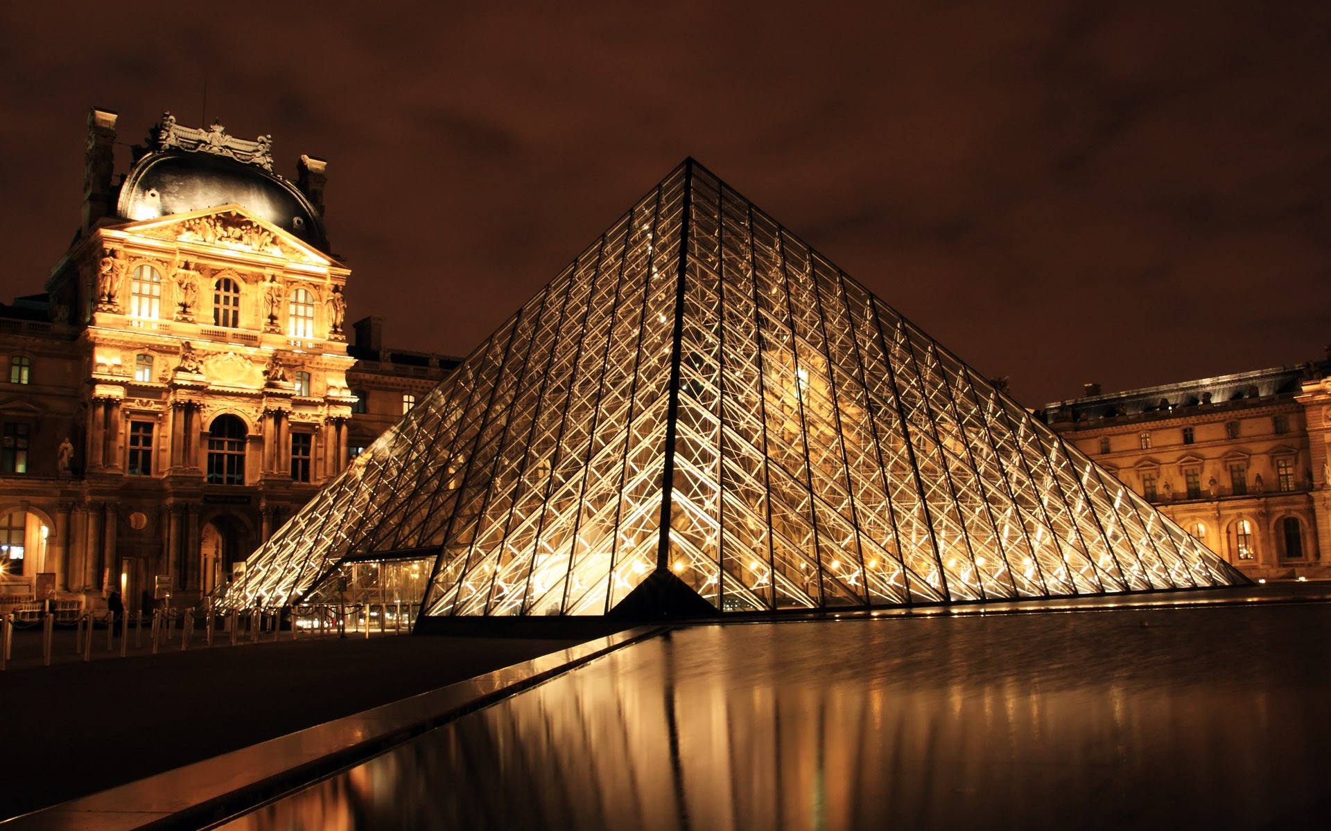 France 桌布 壁紙 — 夜晚，一座發光的玻璃金字塔在濕漉漉的廣場上倒映，旁邊是一座宏偉的燈光新古典主義建築。