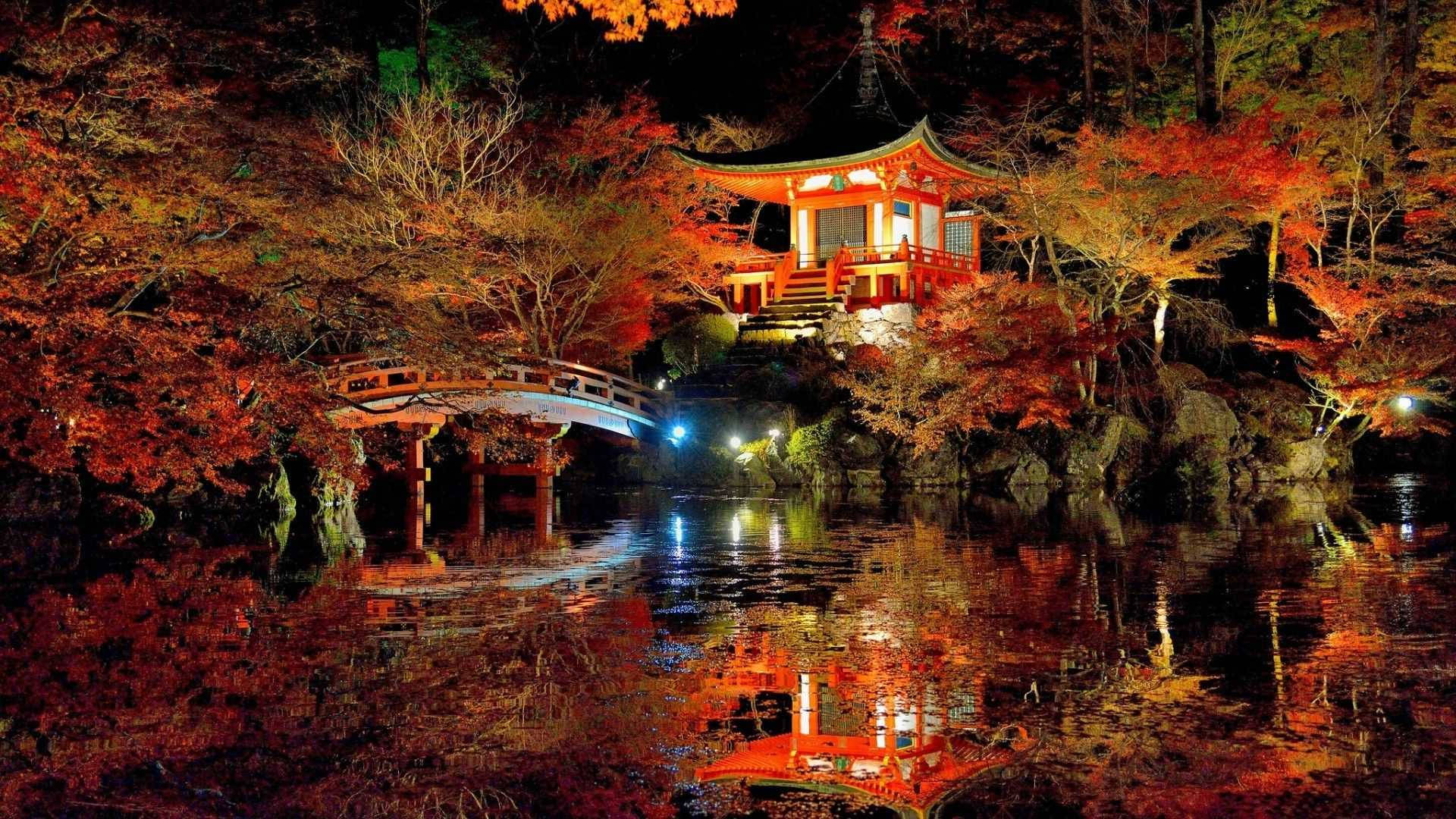 日式自然壁紙 桌布 壁紙 — 夜晚，一座發光的紅色日本寺廟和拱橋倒映在平靜的水面上，上方是火紅的秋樹。