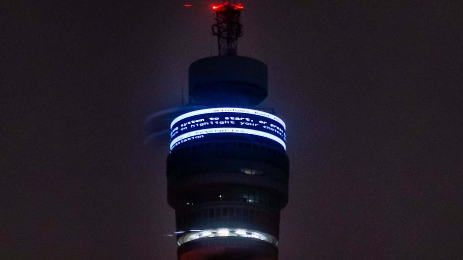 tower 桌布 壁紙 — 夜晚，一座高塔在黑暗的天空中顯示類似Windows啟動畫面的發光藍色文字。