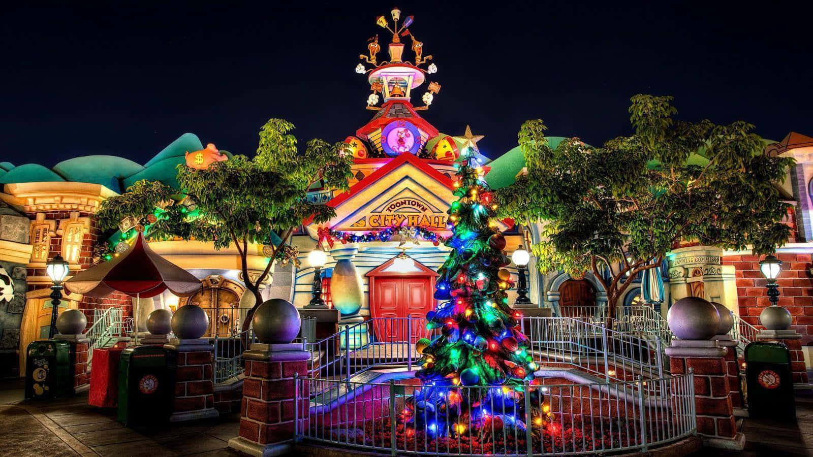 Disneyland 桌布 壁紙 — 夜晚，一棵明亮照明的聖誕樹矗立在色彩繽紛的Dooney市政廳大樓前，周圍環繞著節日裝飾和閃爍的燈光。