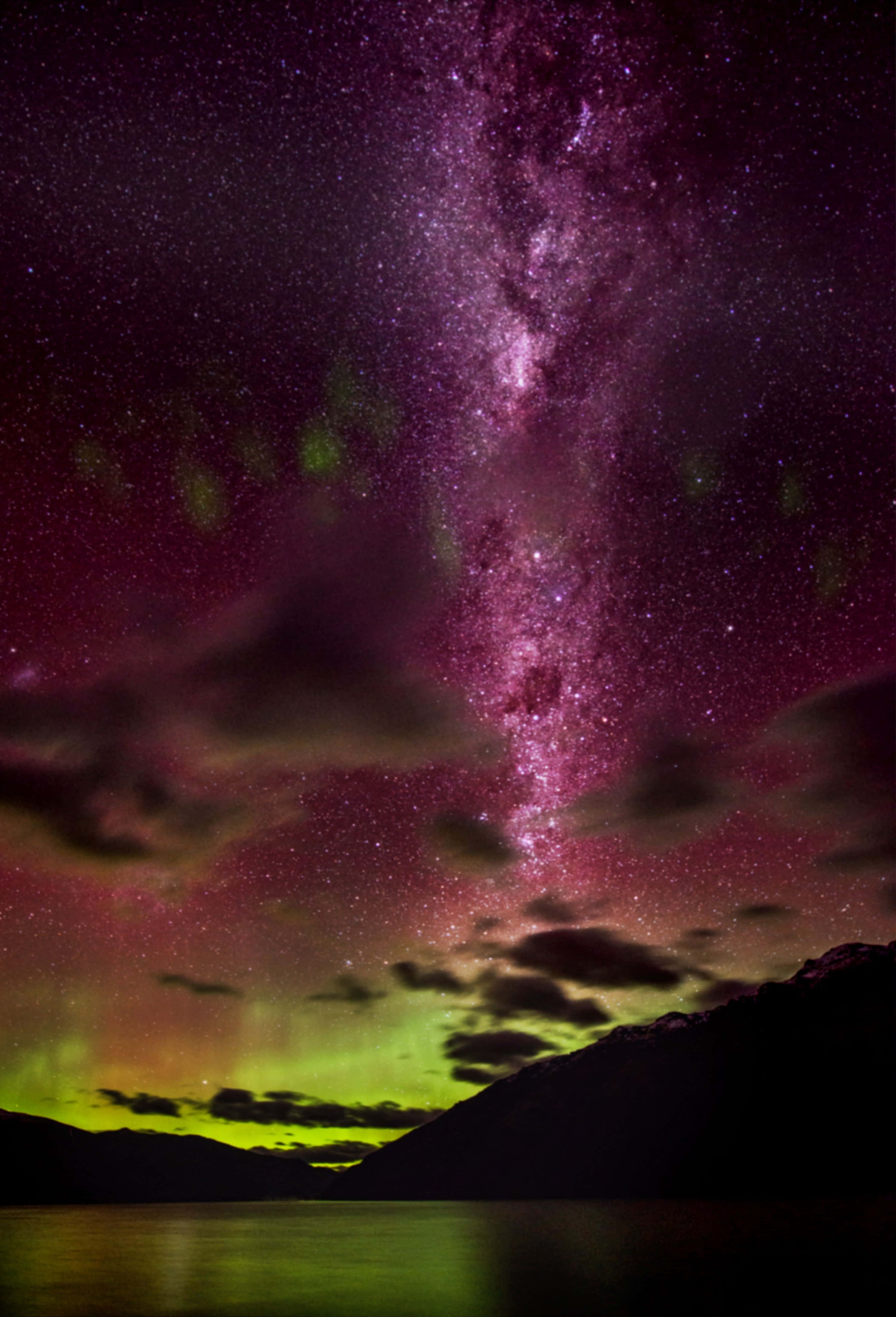 Aurora 桌布 壁紙 — 夜晚，一道充滿活力的紫色和綠色極光在繁星點點的銀河上方舞動，銀河拱跨在黑暗的山間湖泊之上。