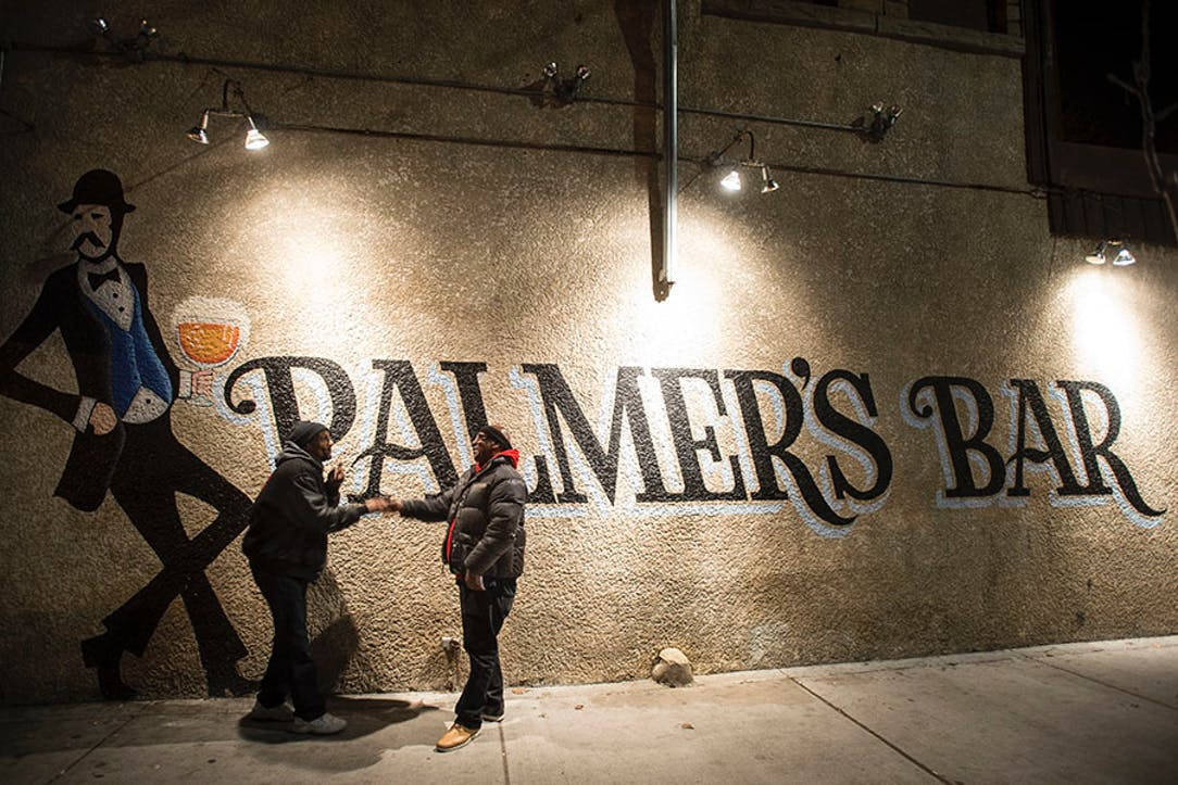 Minneapolis 桌布 壁紙 — 夜晚，兩人在溫暖照明的 Palmer's Bar 壁畫前握手。