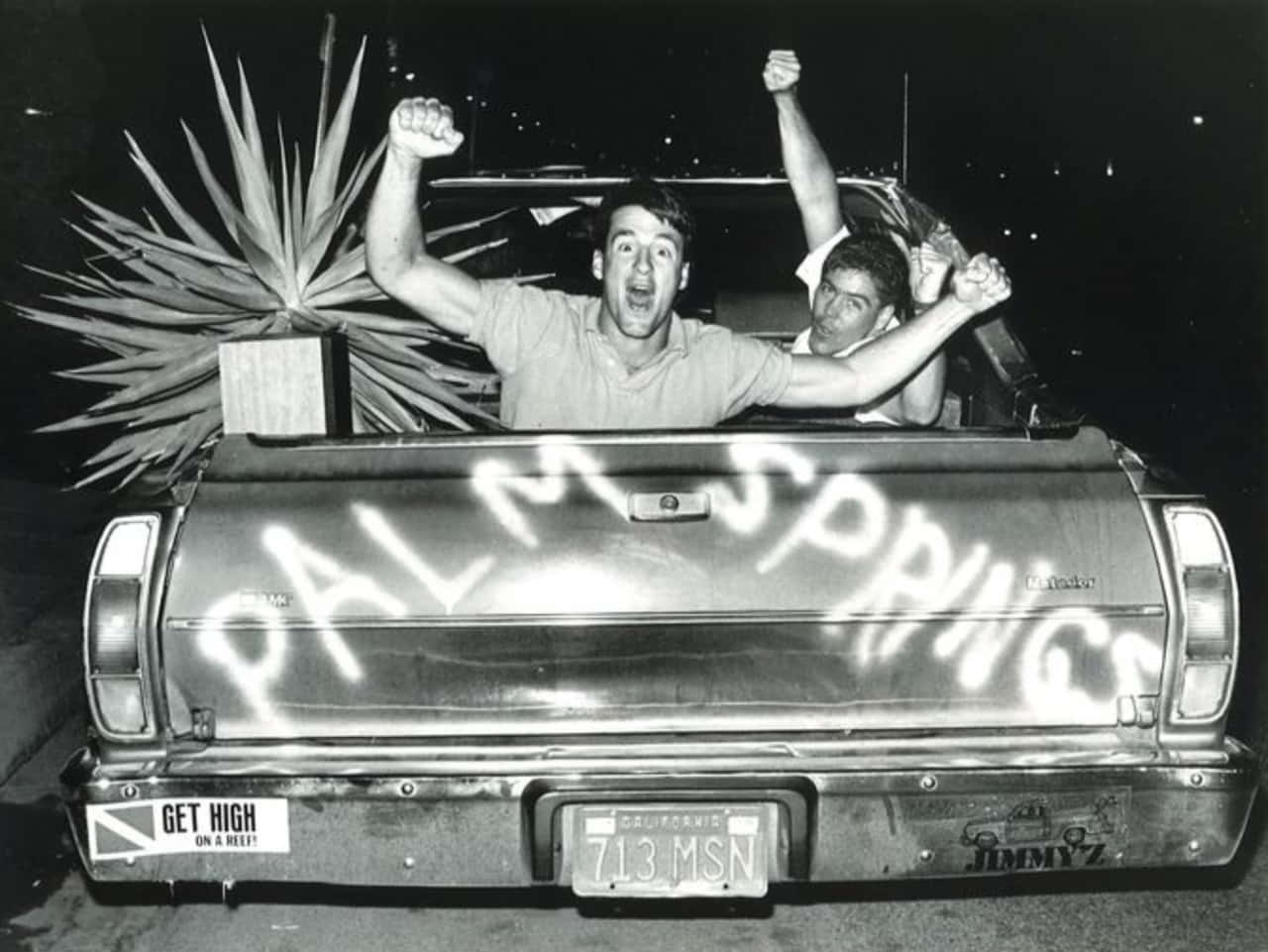 1980s 桌布 壁紙 — 夜晚，兩名男子從皮卡車的車斗中高興地舉起拳頭，尾門上噴有「PALM SPRINGS」字樣。