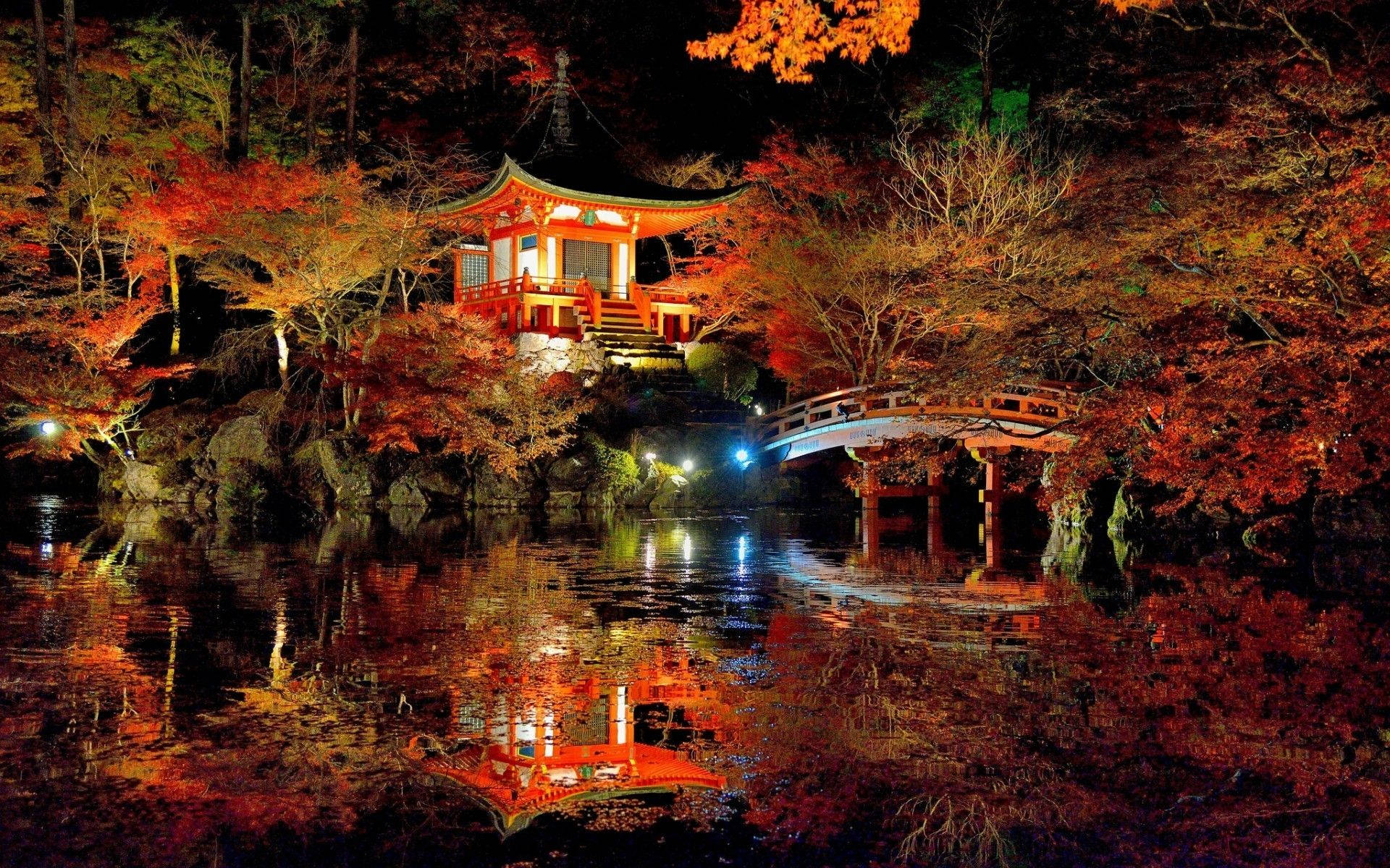 夜晚，被秋葉環繞的水面上倒映著一座燈火通明的日本寺廟和橋樑。