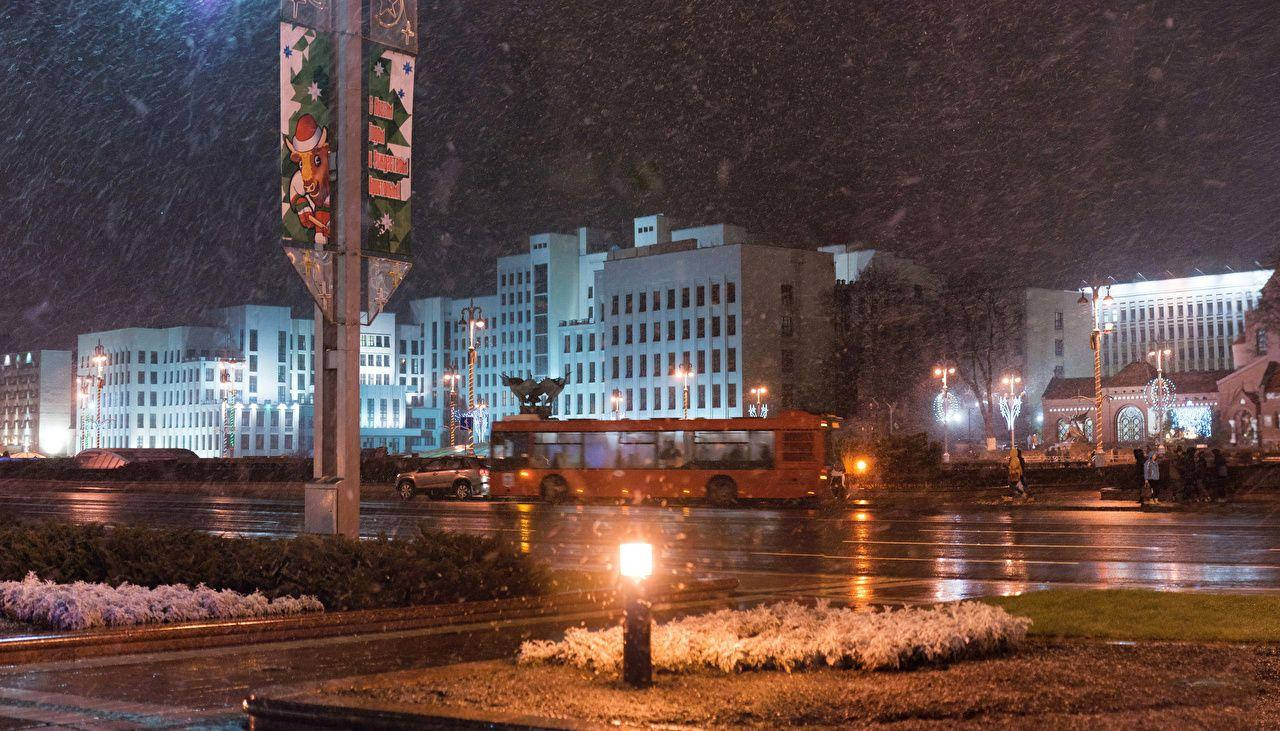 城市 桌布 壁紙 — 夜晚，大雪覆蓋濕漉漉的城市街道，一輛紅色巴士在閃爍的路燈和節日標誌下駛過。