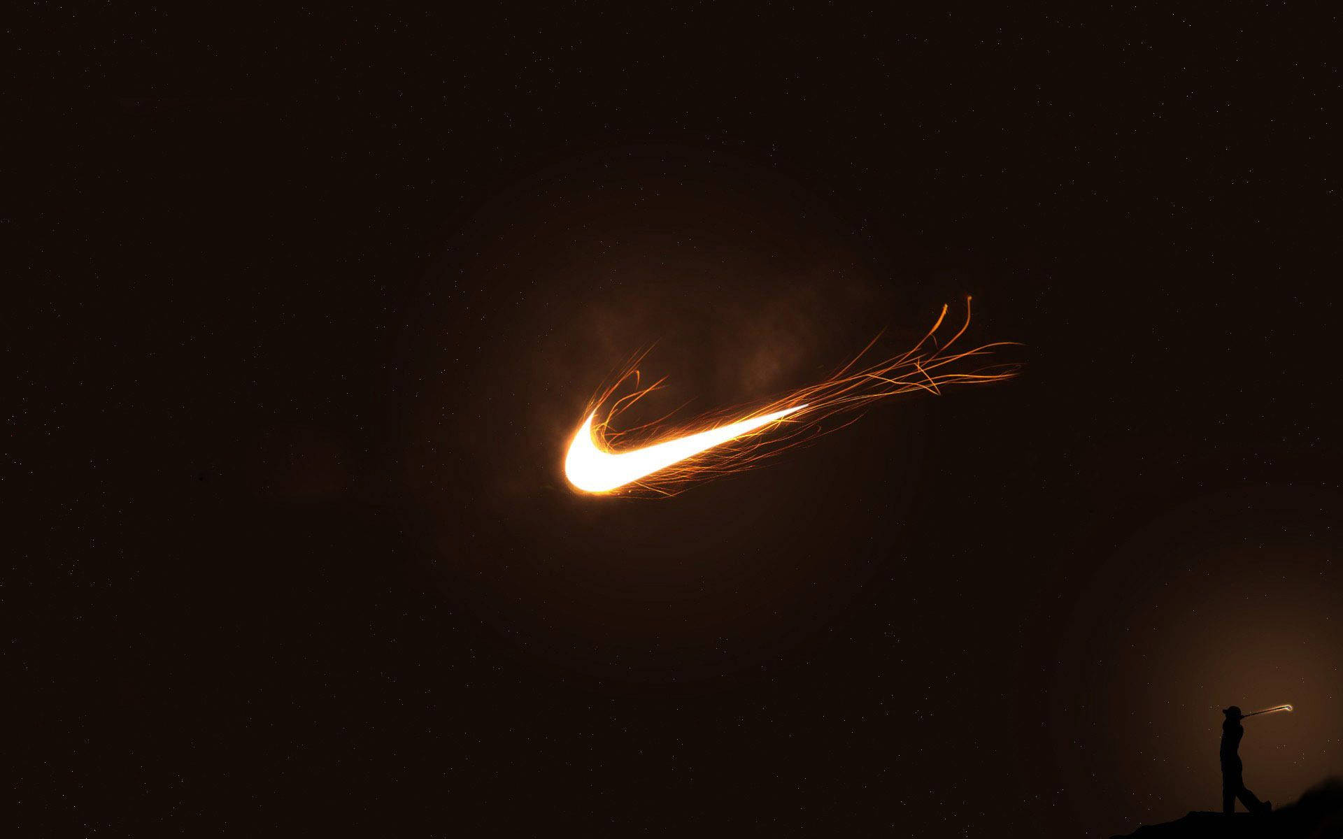 Nike 桌布 壁紙 — 夜晚，懸崖上一個孤獨的身影用煙火棒在星空下創造出發光的Nike勾號。