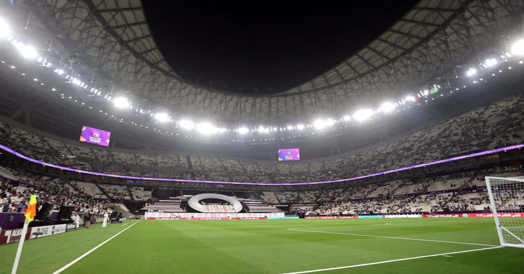 Soccer Stadium 桌布 壁紙 — 夜晚一個廣闊的照明足球場，閃爍的燈光和擠滿的人群圍繞著充滿活力的綠色球場。