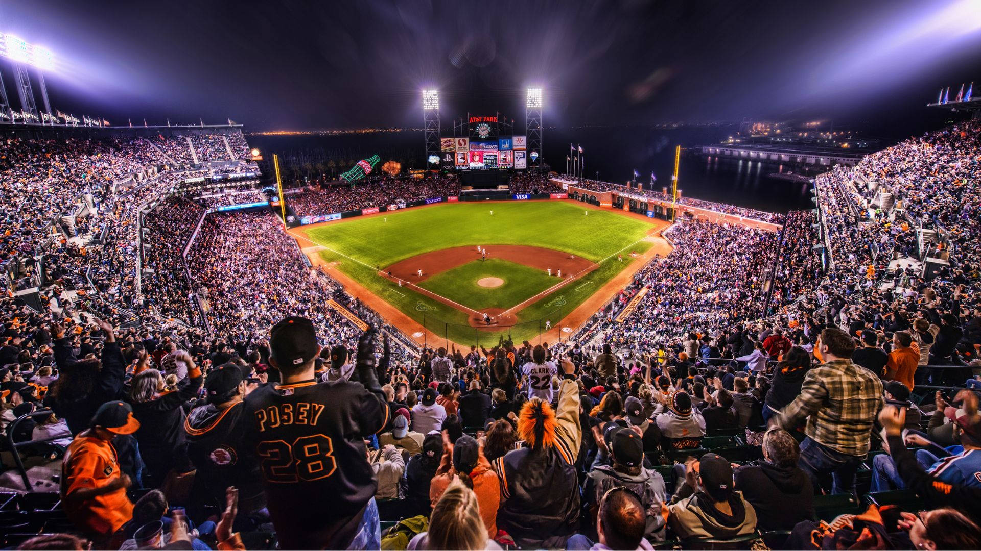 Giants 桌布 壁紙 — 夜晚一個擠滿人的棒球場，球迷在明亮的燈光下歡呼，圍繞著充滿活力的綠色場地。
