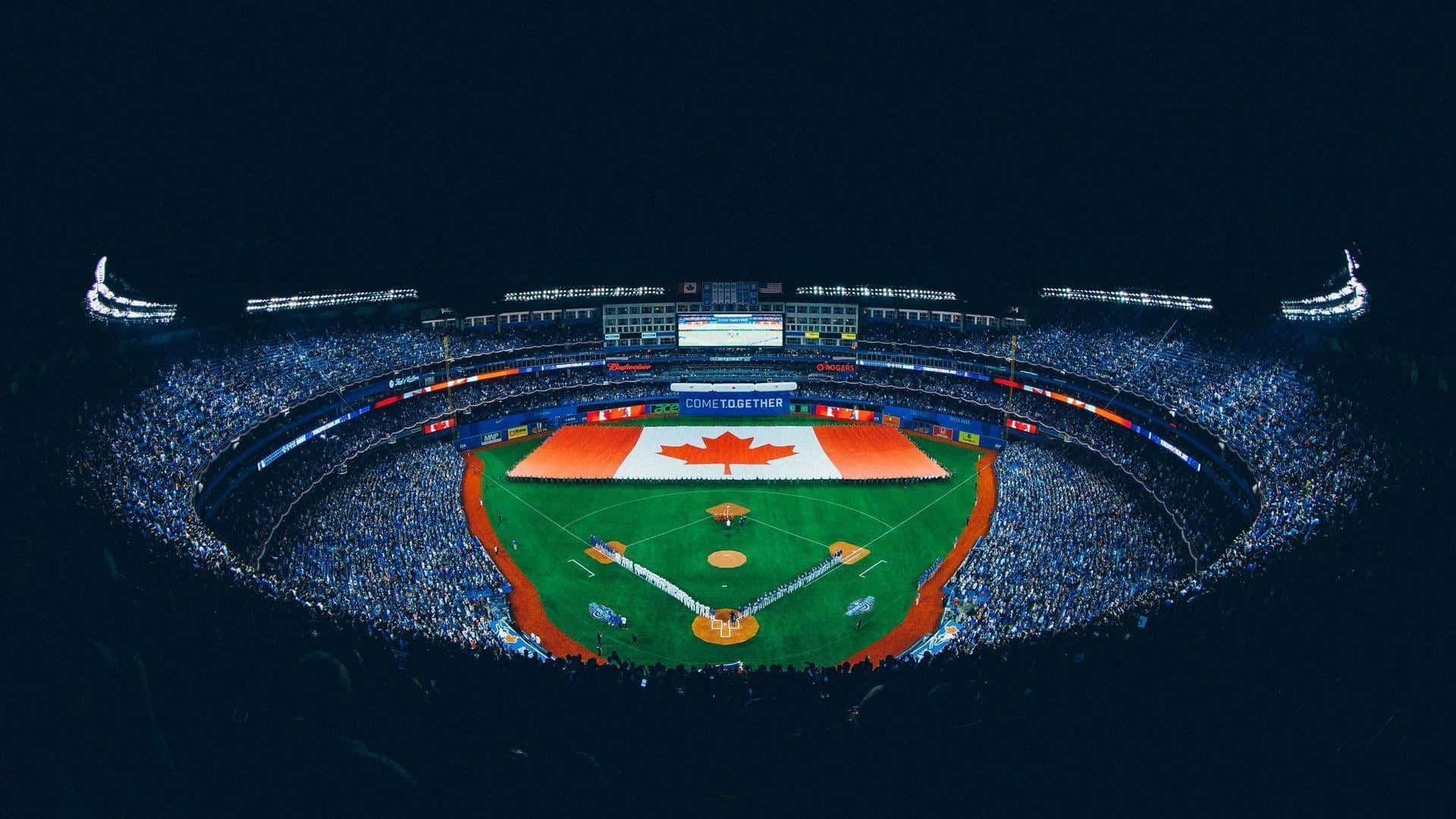 Blue Jays. 桌布 壁紙 — 夜晚一個擠滿人的棒球場的鳥瞰圖，場地上有一面巨大的加拿大國旗，發光的藍色燈光照亮了人群。