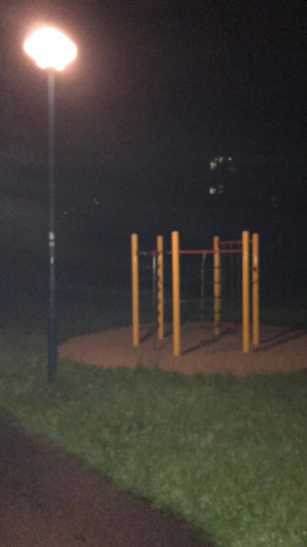 夢核 桌布 壁紙 — 夜晚一個昏暗的戶外健身站，由單一街燈照亮，在草地和泥土上投下長長的影子。