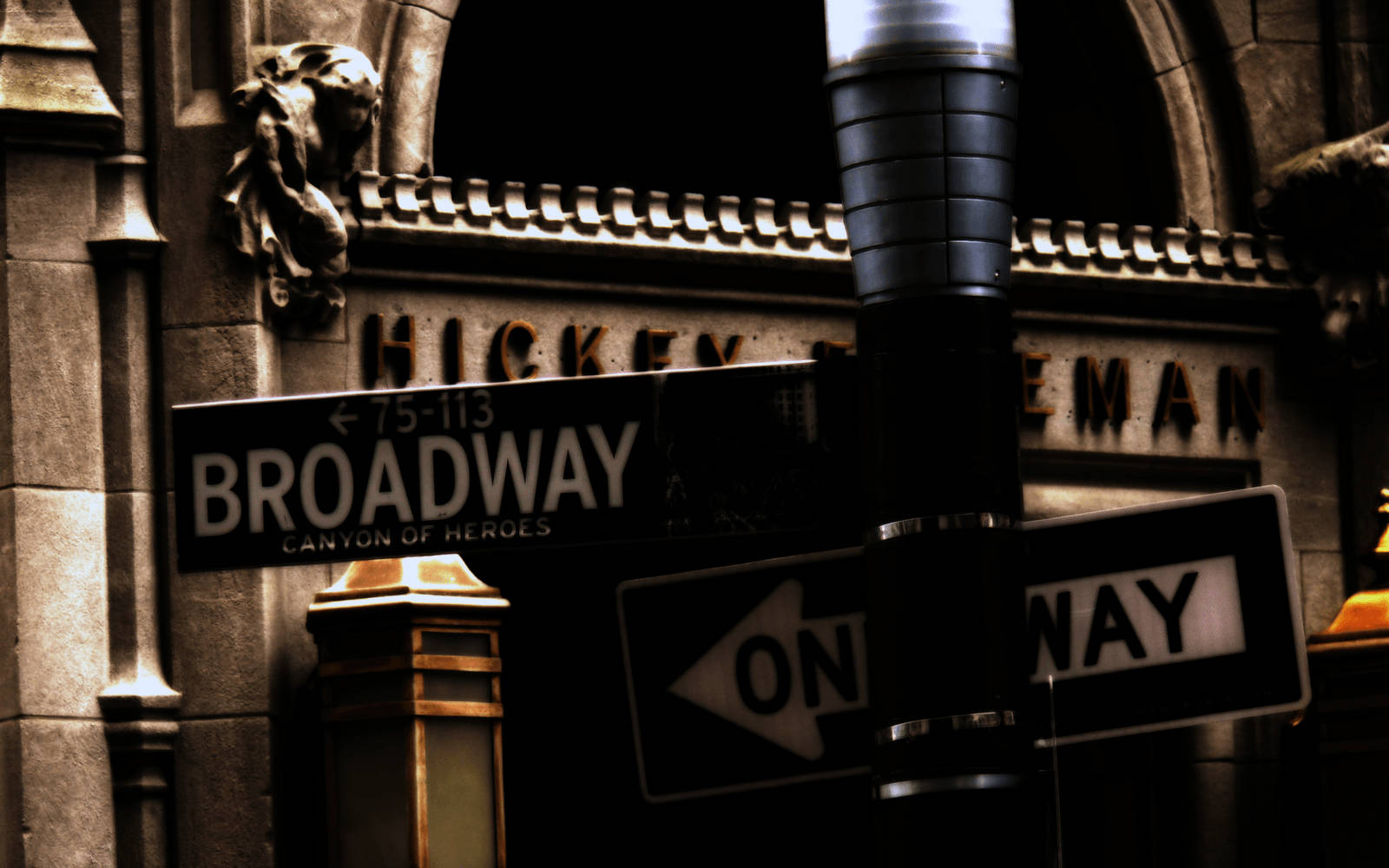 Broadway 桌布 壁紙 — 夜晚一個粗糙的城市街角，有 Broadway 標誌和單向箭頭，背景是石頭建築外牆。