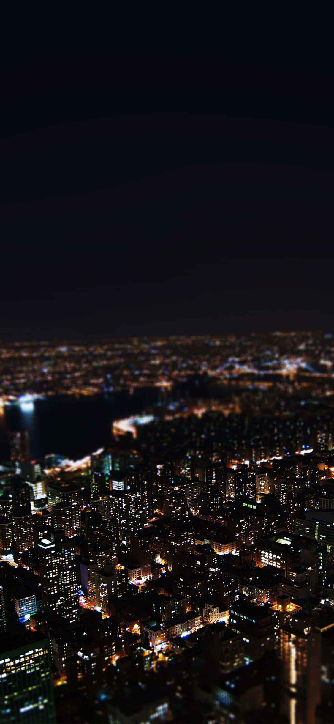 New York City Night iPhone 桌布 壁紙 — 夜晚一座廣闊城市的模糊鳥瞰圖，燈光閃爍，天空漆黑。