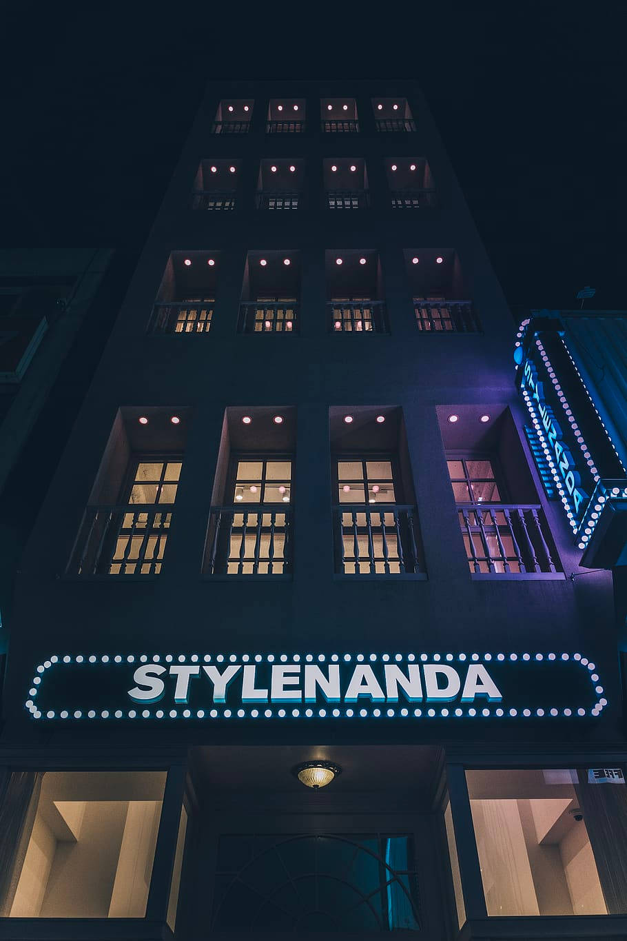 Hotel 桌布 壁紙 — 夜晚一座高聳的建築物被發光的窗戶和明亮的「STYLENANDA」招牌照亮。