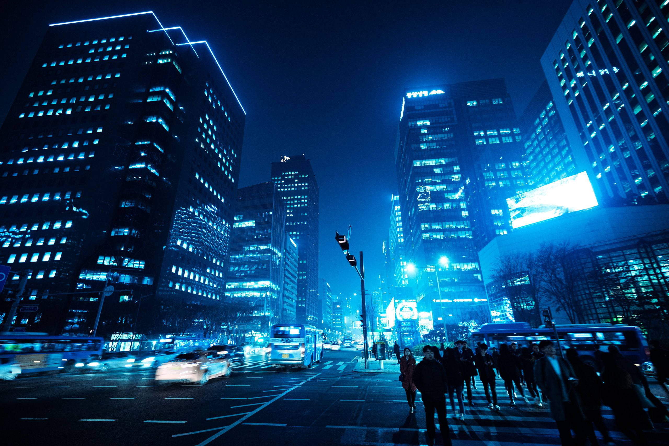 lights 桌布 壁紙 — 夜晚一條充滿活力的藍色霓虹燈城市街道，高聳的摩天大樓閃閃發光，汽車和行人的模糊運動。