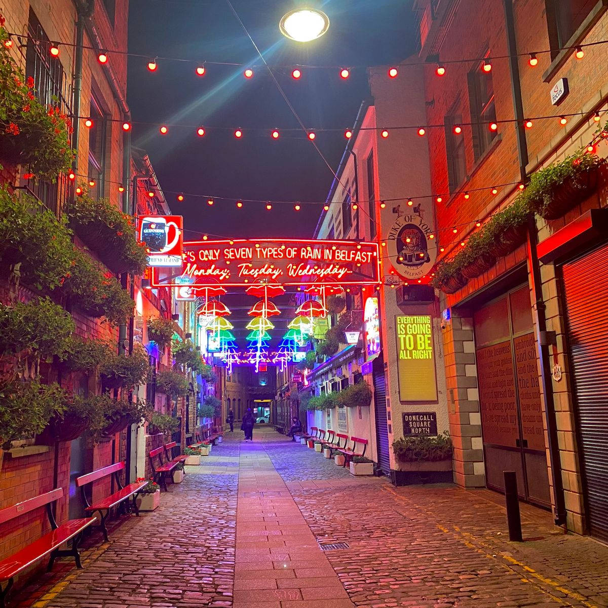 聖誕燈飾 桌布 壁紙 — 夜晚一條充滿活力的霓虹燈小巷，掛燈、彩色招牌和磚砌建築營造出熱鬧的城市氛圍。