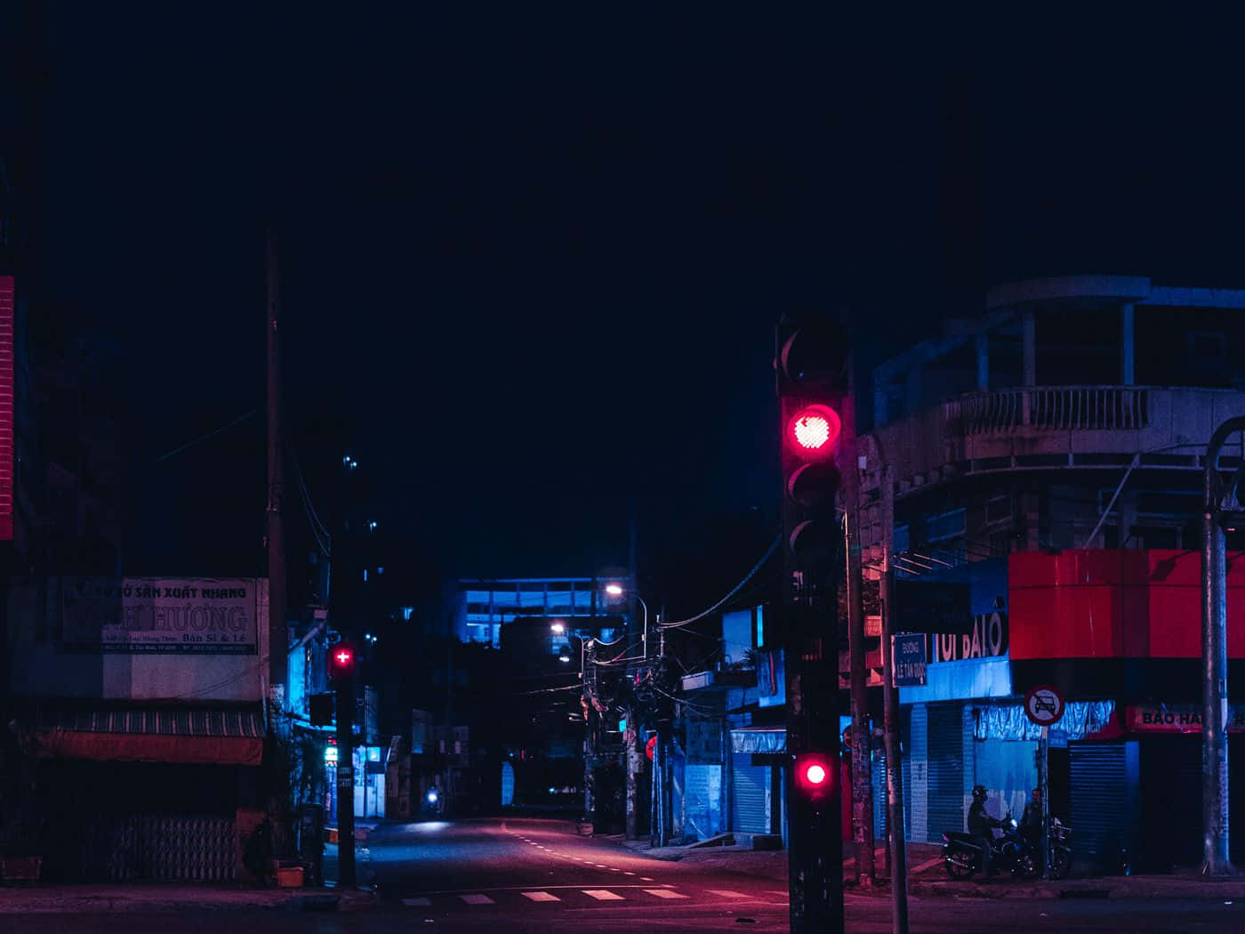 紅色動圖 桌布 壁紙 — 夜晚一條充滿霓虹燈的城市街道，紅色交通燈在濕漉漉的人行道和關閉的商店門面上投射出超現實的光芒。