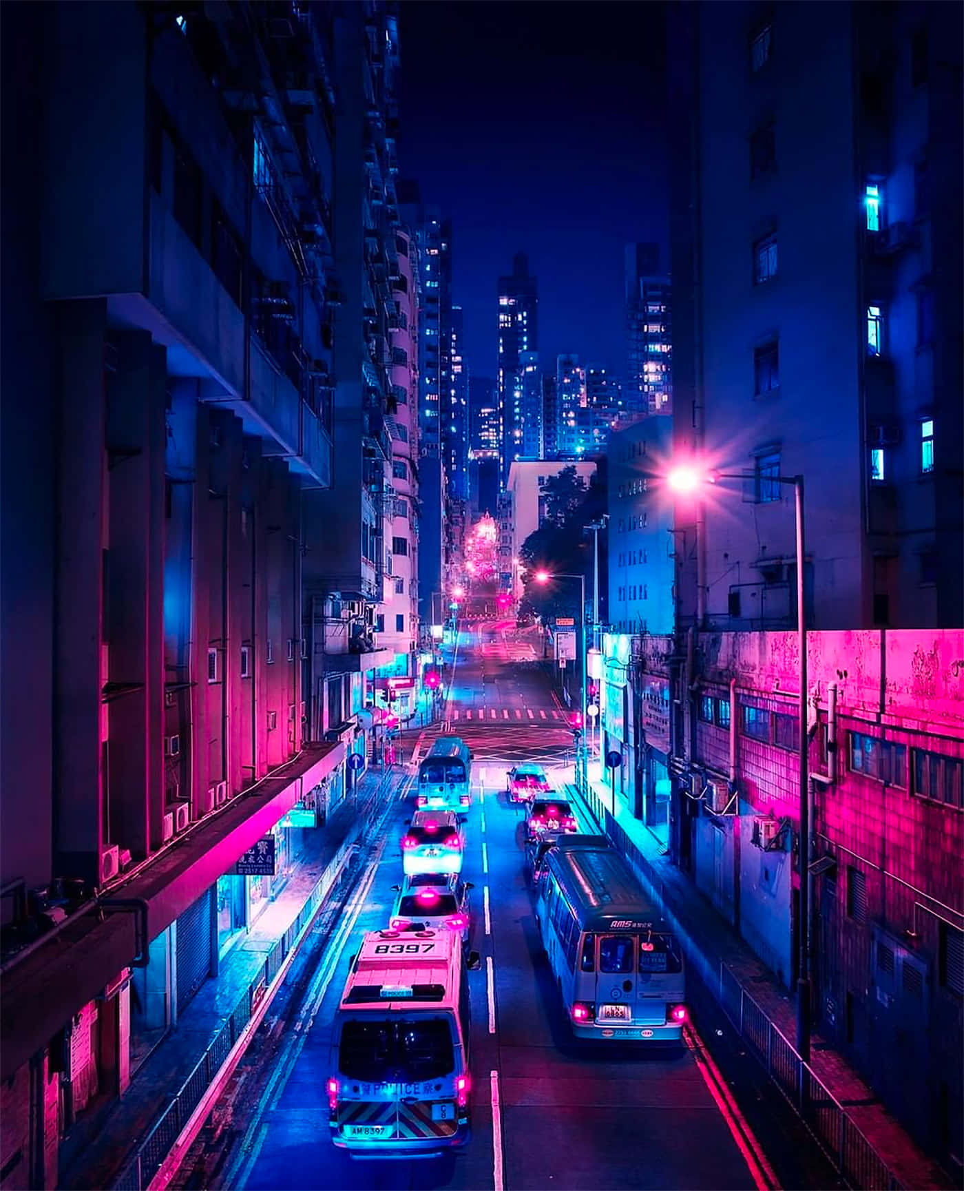 夜晚 桌布 壁紙 — 夜晚一條充滿霓虹燈的都市小巷，粉紅色和藍色的燈光在潮濕的路面上反射，巴士和汽車在高聳的建築物之間穿梭。
