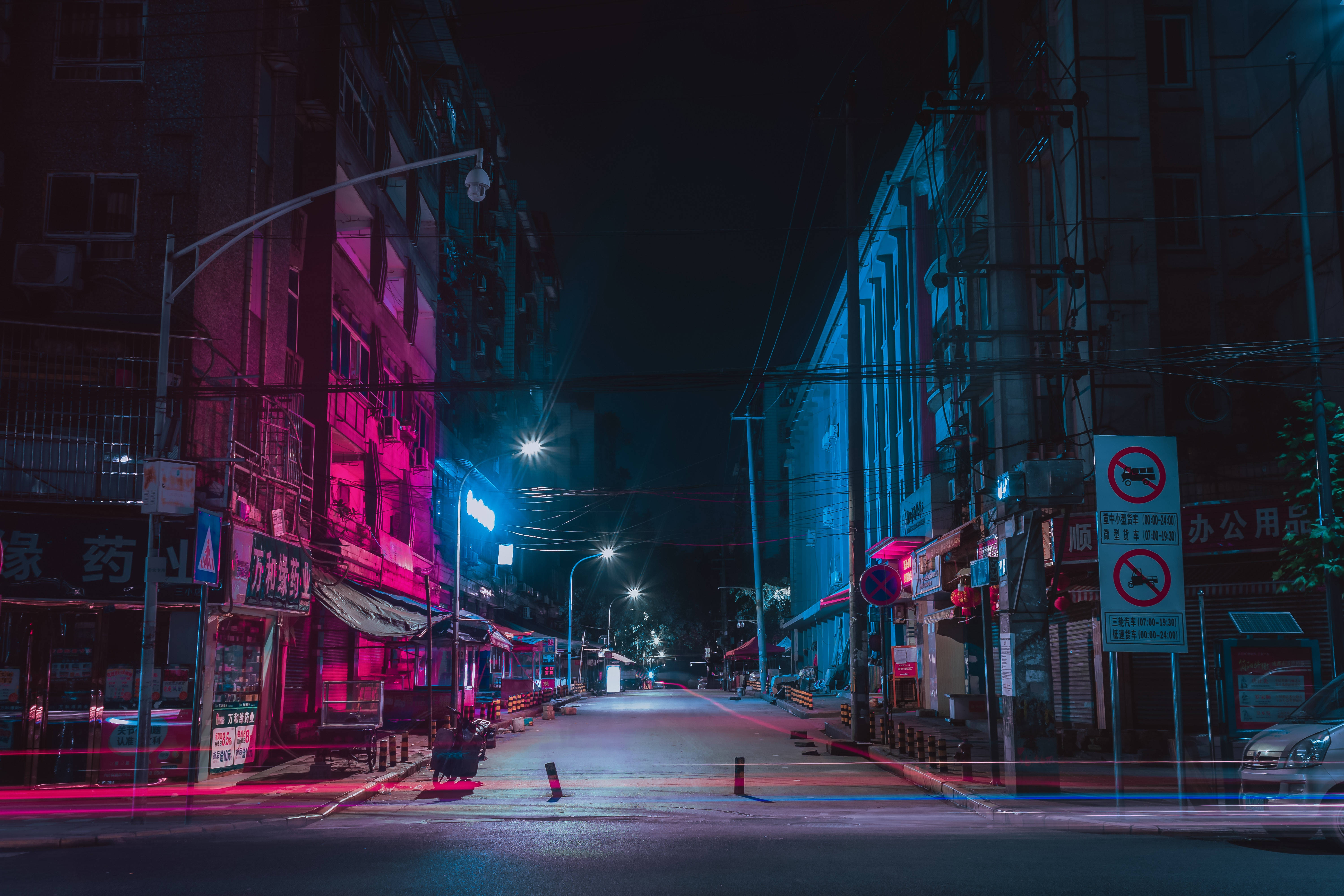 Street 桌布 壁紙 — 夜晚一條充滿霓虹燈的都市小巷，粉紅色和藍色的燈光反射在濕漉漉的路面上，頭頂的電線縱橫交錯。