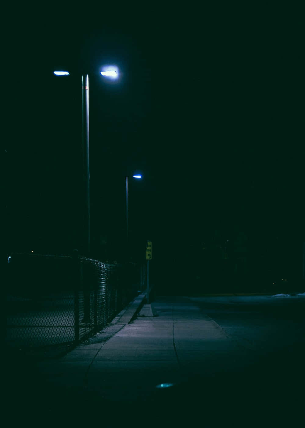 夜晚 桌布 壁紙 — 夜晚一條昏暗的人行道，被冰冷的藍色路燈照亮，在鐵絲網上投下長長的影子。