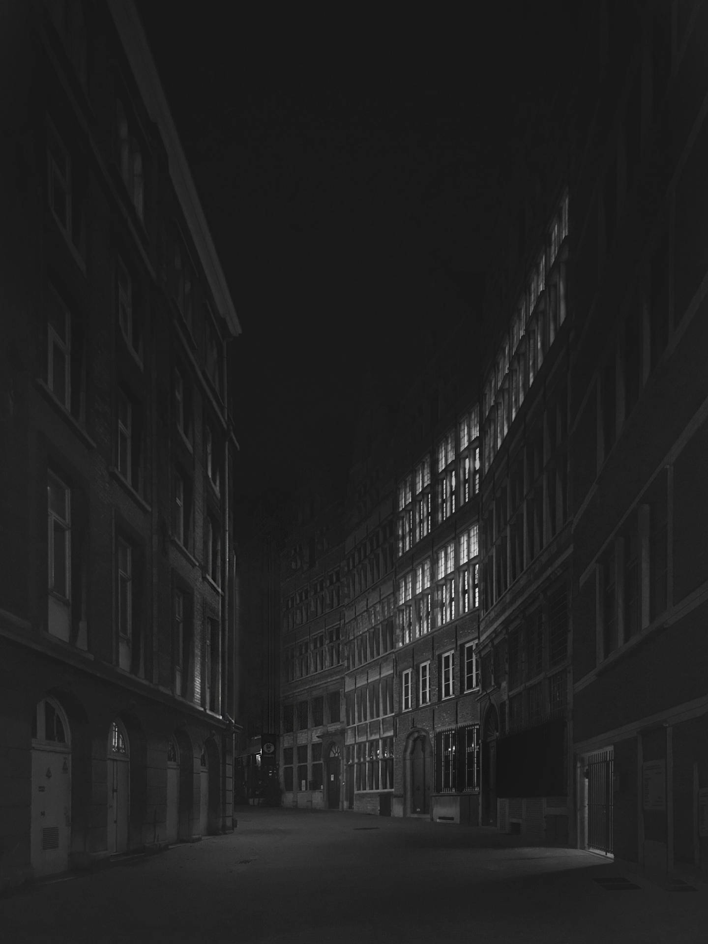 夜晚黑暗的城市小巷，高樓大廈中有明亮的窗戶。 — 極簡黑色手機桌布 壁紙