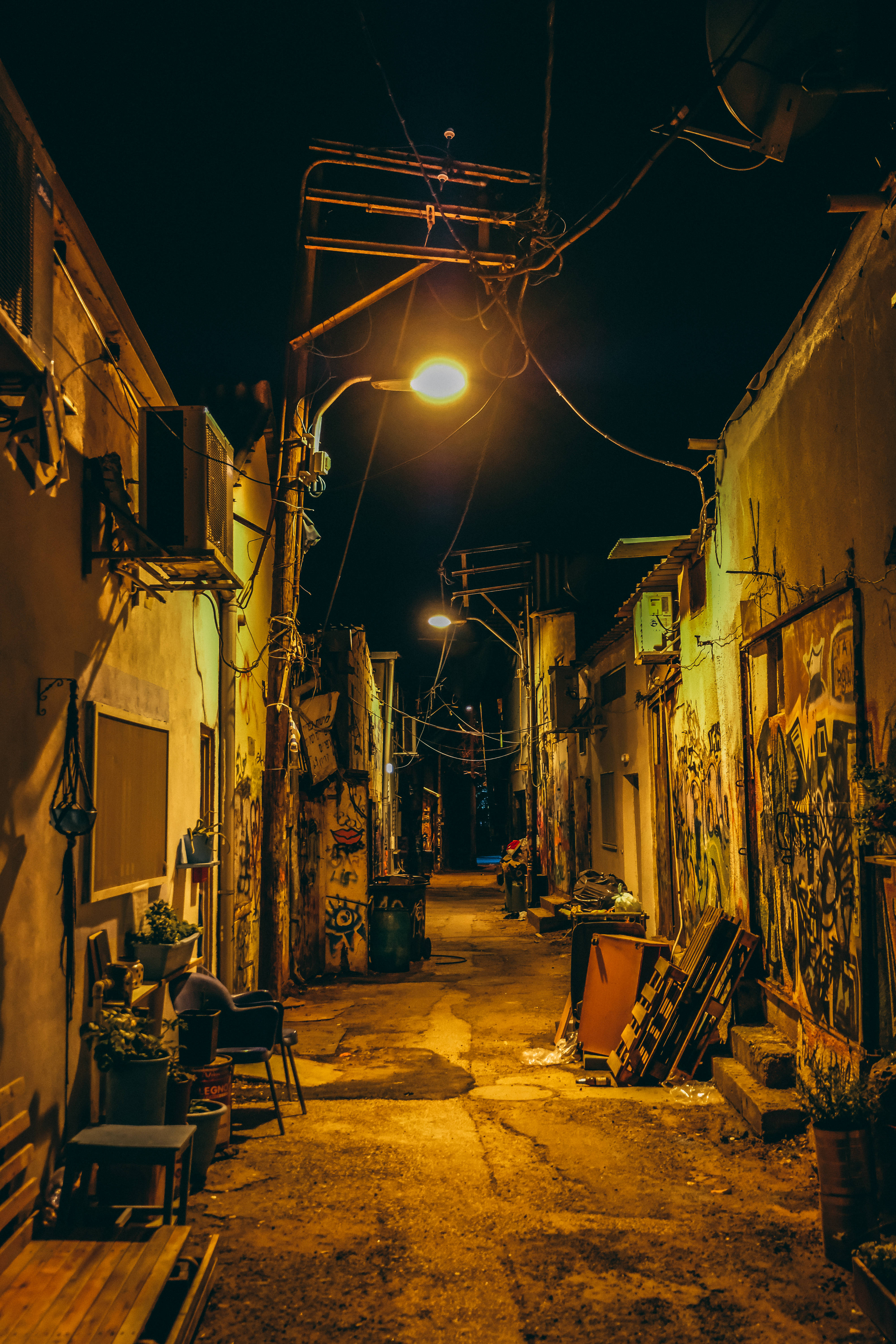 街頭 桌布 壁紙 — 夜晚一條狹窄的城市小巷，被一盞溫暖的路燈照亮，在塗鴉覆蓋的牆壁和雜亂的碎片上投下長長的陰影。