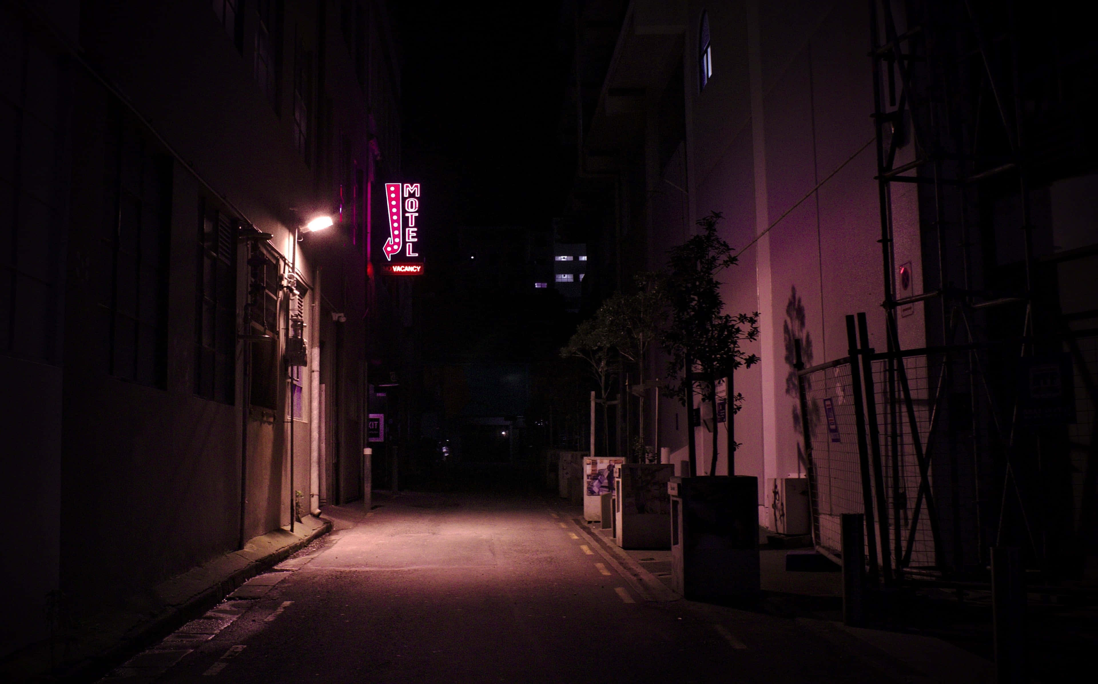neon sign 桌布 壁紙 — 夜晚一條狹窄的城市小巷，被發光的粉紅色霓虹燈汽車旅館招牌照亮，在潮濕的路面上投射出超現實的光芒。