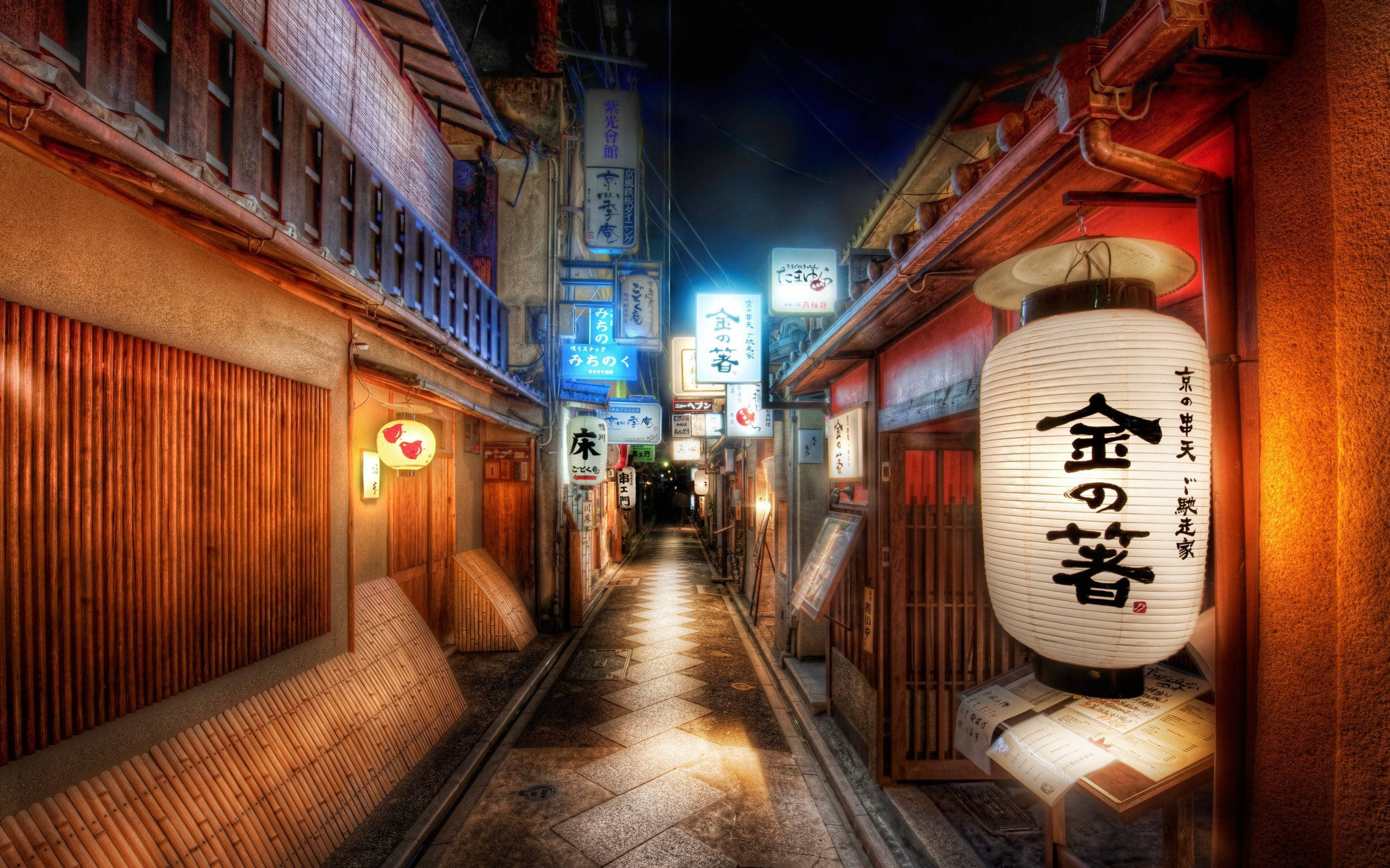 唐人街 桌布 壁紙 — 夜晚一條狹窄的日本小巷，被發光的燈籠和霓虹燈招牌照亮，倒映在濕漉漉的石板路上。