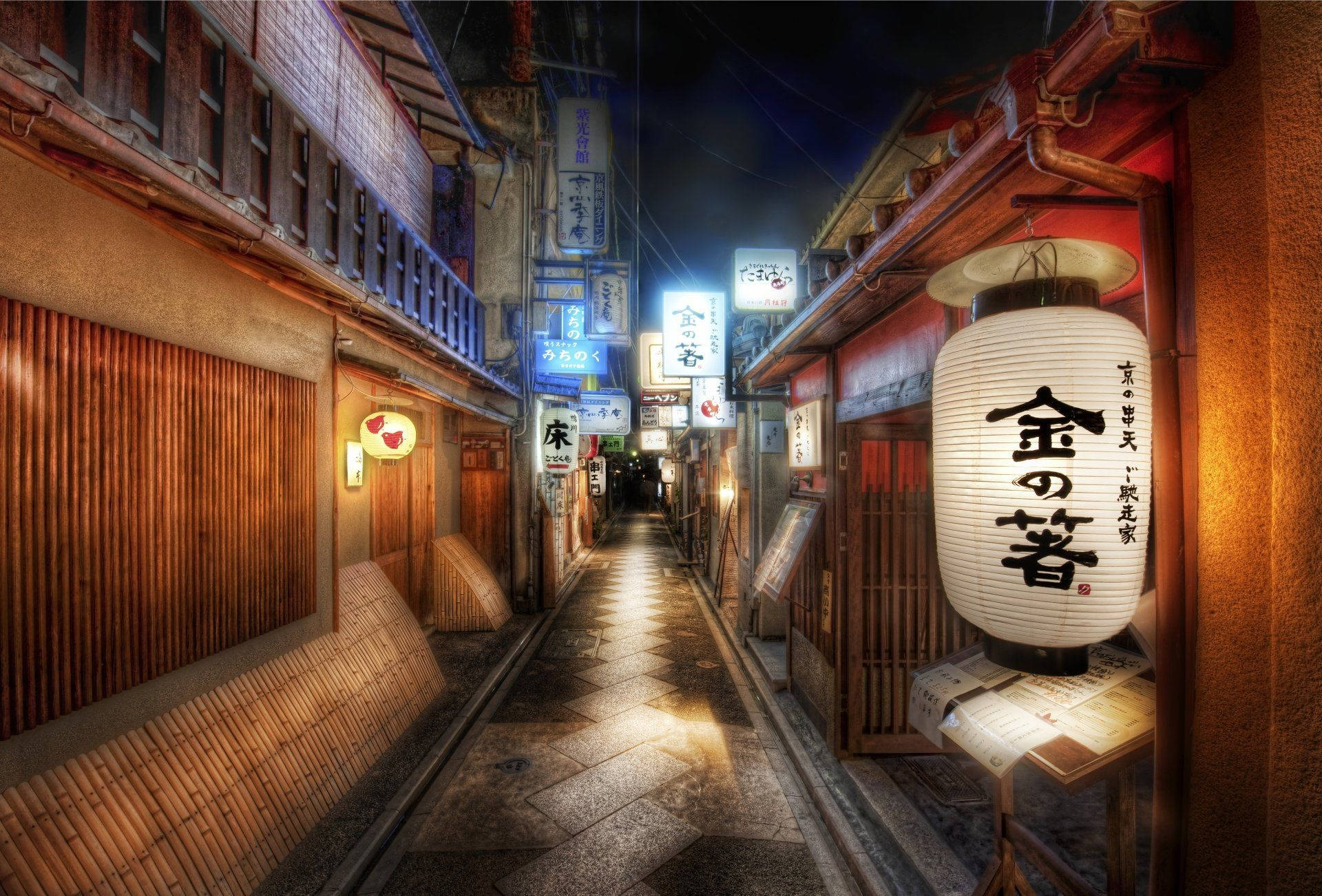 京都 桌布 壁紙 — 夜晚一條狹窄的日本小巷，被發光的燈籠和霓虹燈照亮，倒影在濕漉漉的石板路上。
