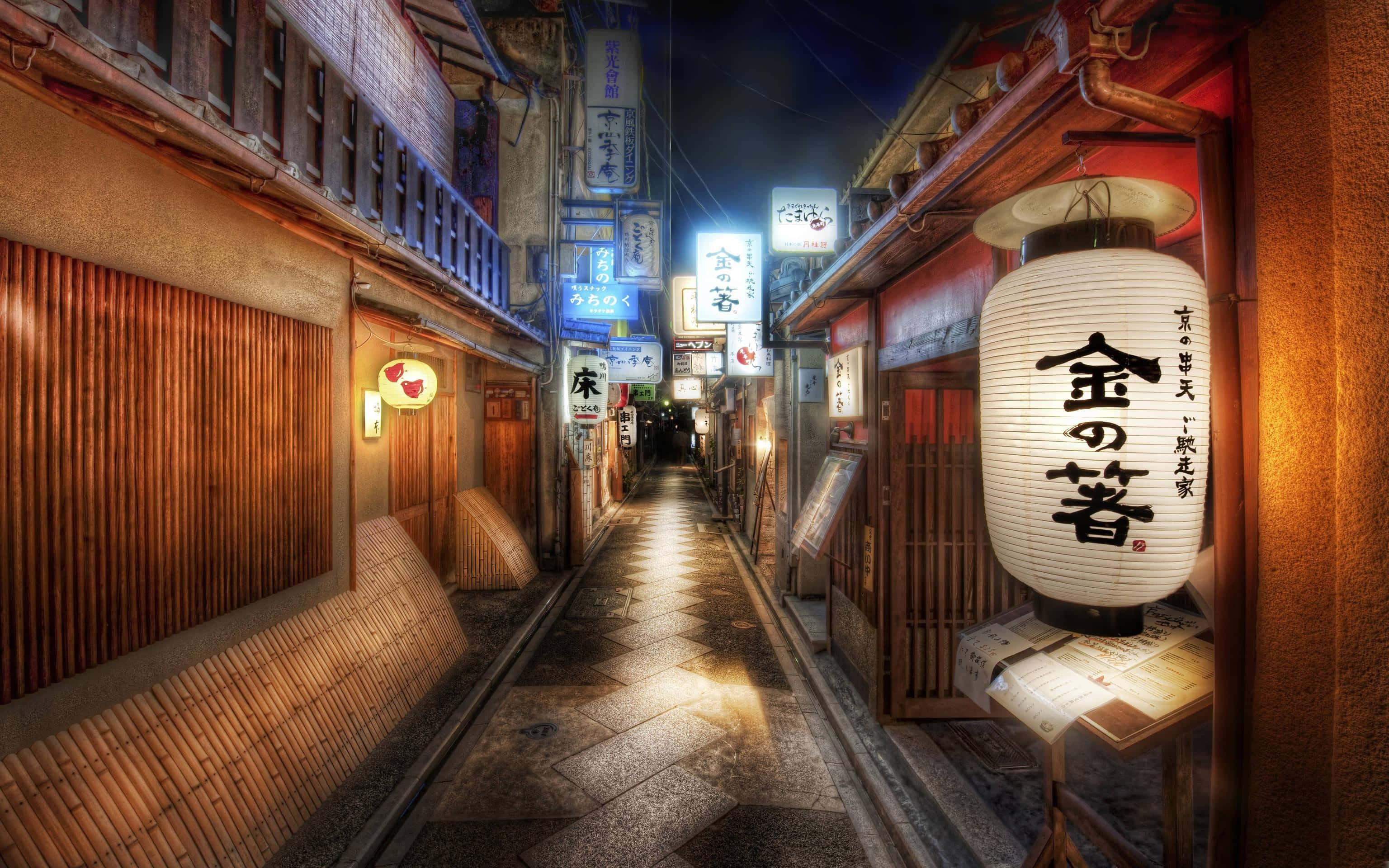 日本 桌布 壁紙 — 夜晚一條狹窄的日本小巷，被發光的燈籠和霓虹燈招牌照亮，倒映在濕漉漉的石板路上。